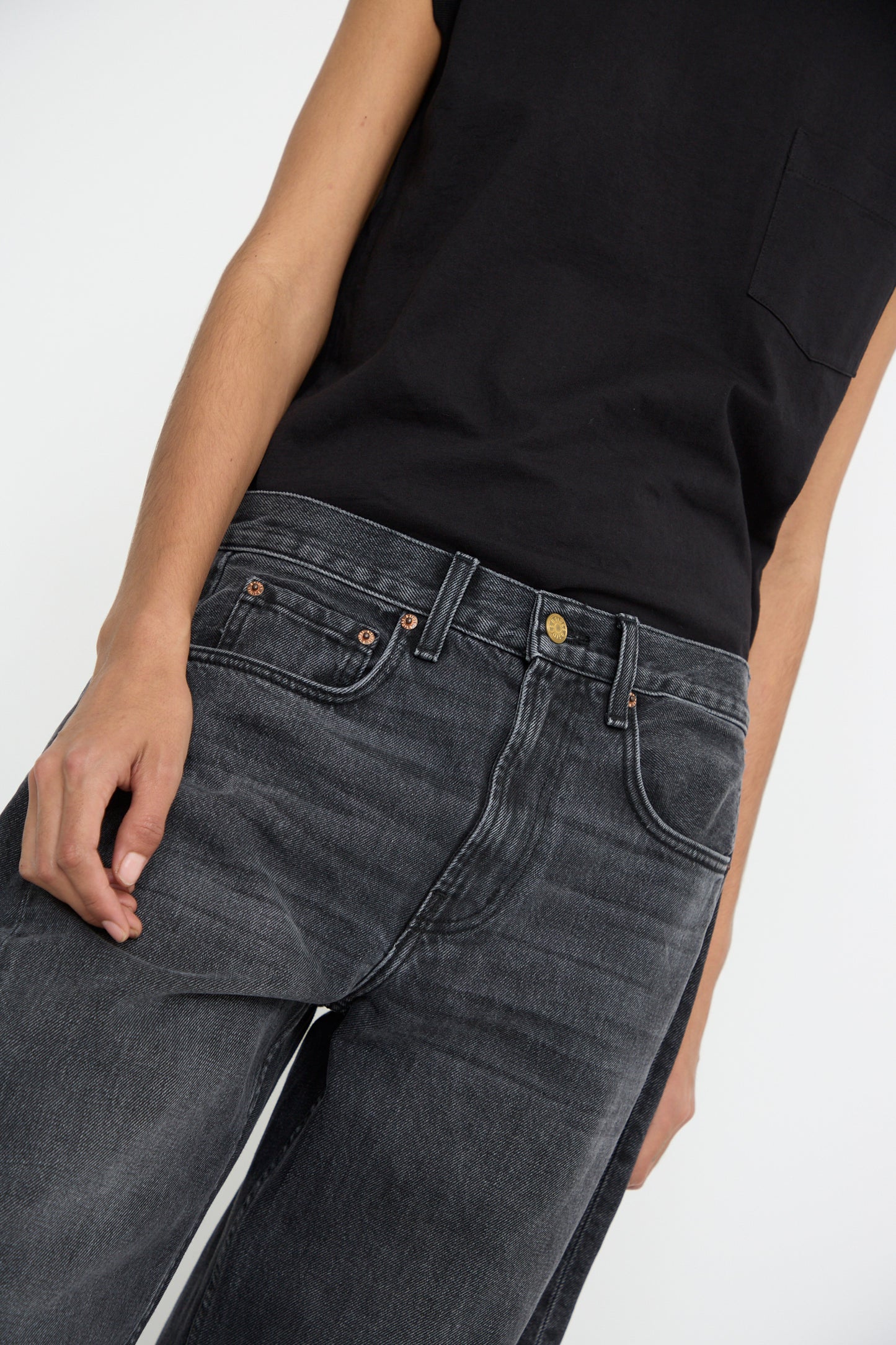 A person wearing a black sleeveless top and the Relaxed Lasso Jean in Stil Black from B Sides, crafted from 100% cotton.