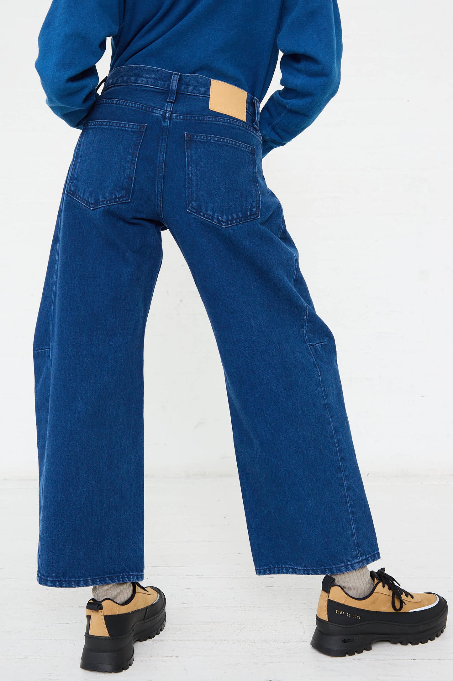 The image displays a person from behind wearing the Relaxed Lasso Jean in Van Blue by B Sides and beige sneakers.