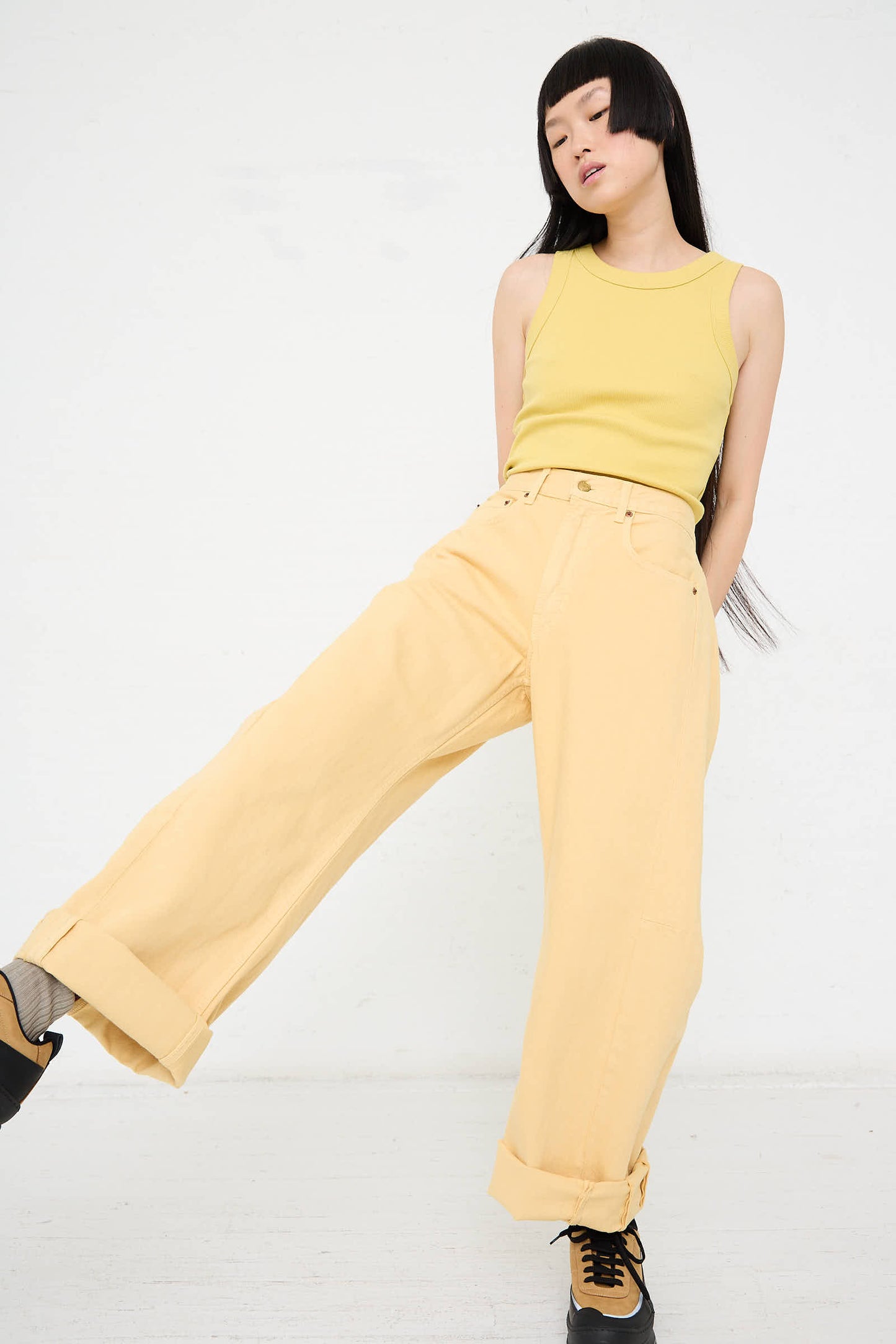 Person wearing a yellow sleeveless top and the Relaxed Lasso Long Jean in Yellow Overdye by B Sides, standing against a plain white background.