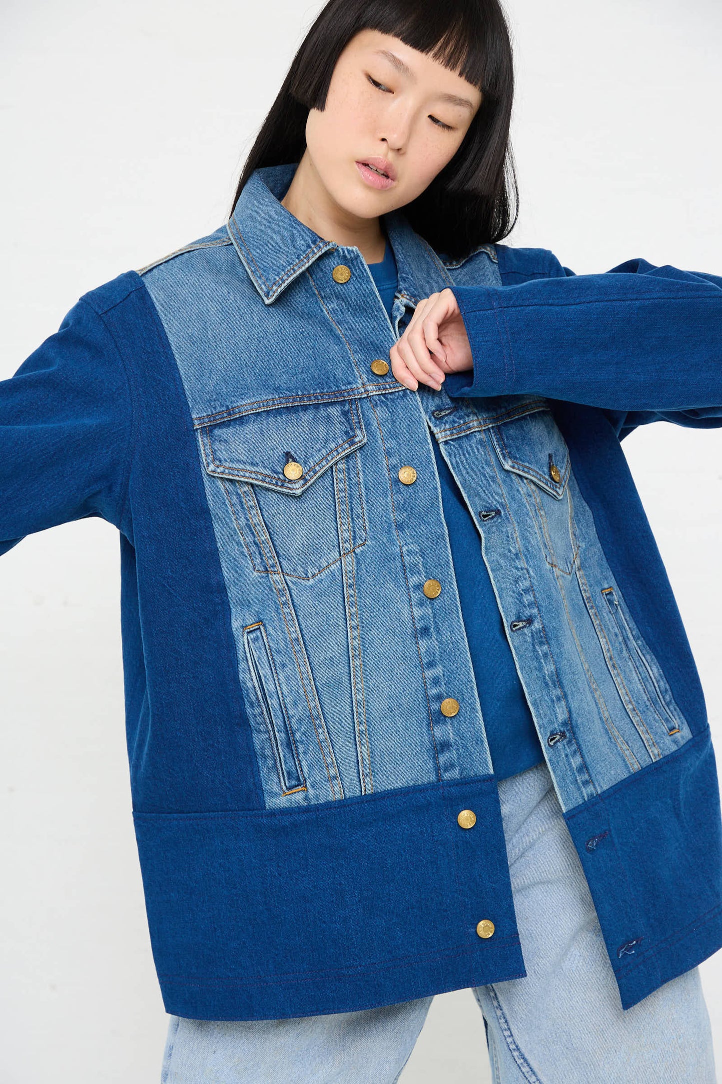 A person with long hair models a relaxed fit Reworked Barn Jacket in Quincy Blue by B Sides, showcasing multiple shades of blue and gold buttons, paired with light blue jeans.