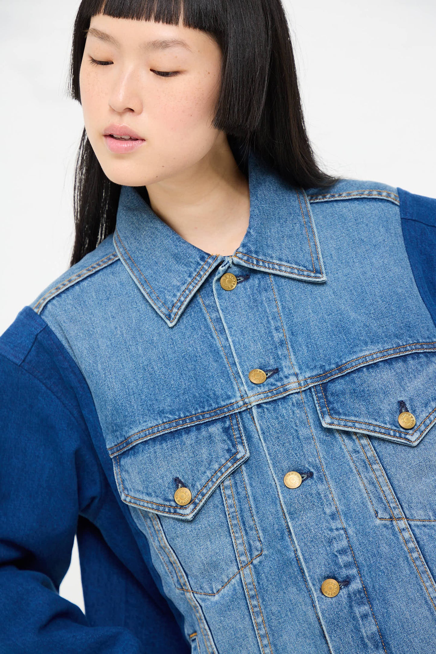 A young person with straight black hair and bangs wears the Reworked Barn Jacket in Quincy Blue by B Sides, showcasing a relaxed fit and contrast sleeves. The person looks down and slightly to the side.