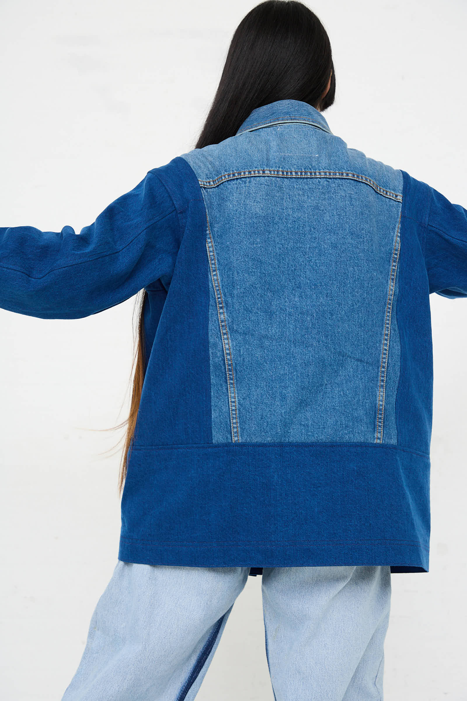 Person with long hair wearing a relaxed fit Reworked Barn Jacket in Quincy Blue from B Sides and light blue jeans, facing away from the camera against a plain background.