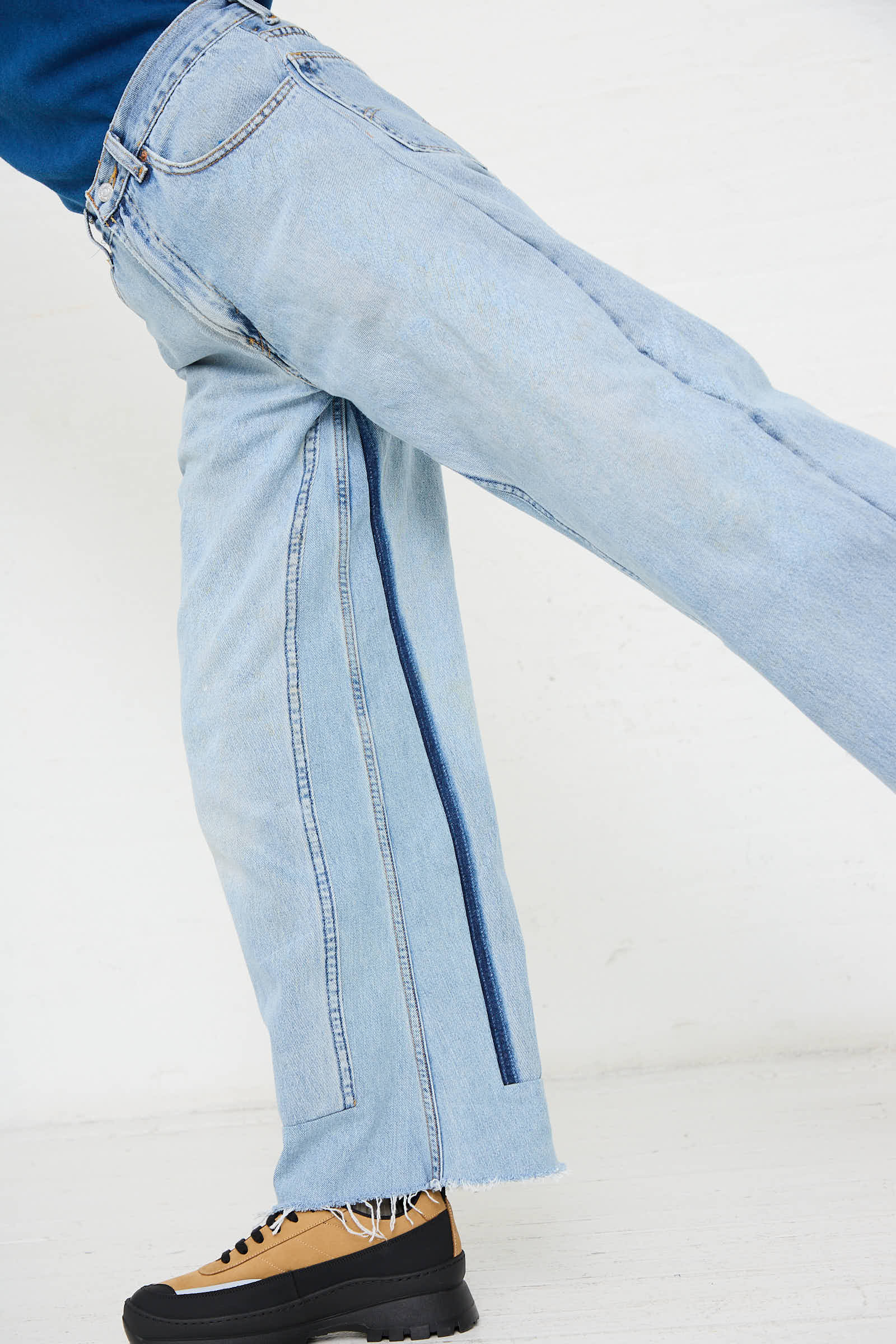 A person wearing B Sides' Reworked Culotte in Vintage Indigo, featuring a dark blue stripe down the side and a raw hem for a vintage denim look, paired with tan and black shoes.