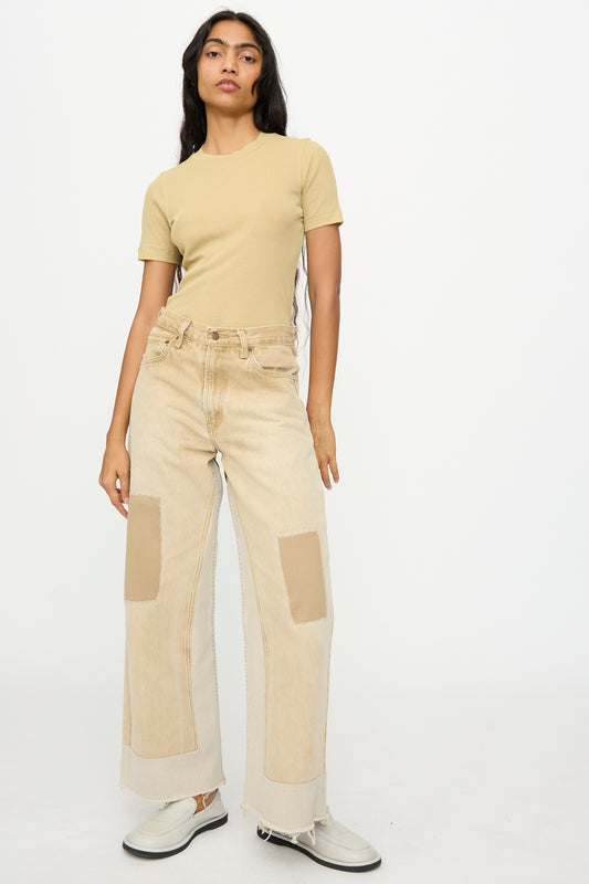 A woman stands against a plain background wearing a beige t-shirt, B Sides Reworked Vintage Culotte in Khaki, and white shoes.