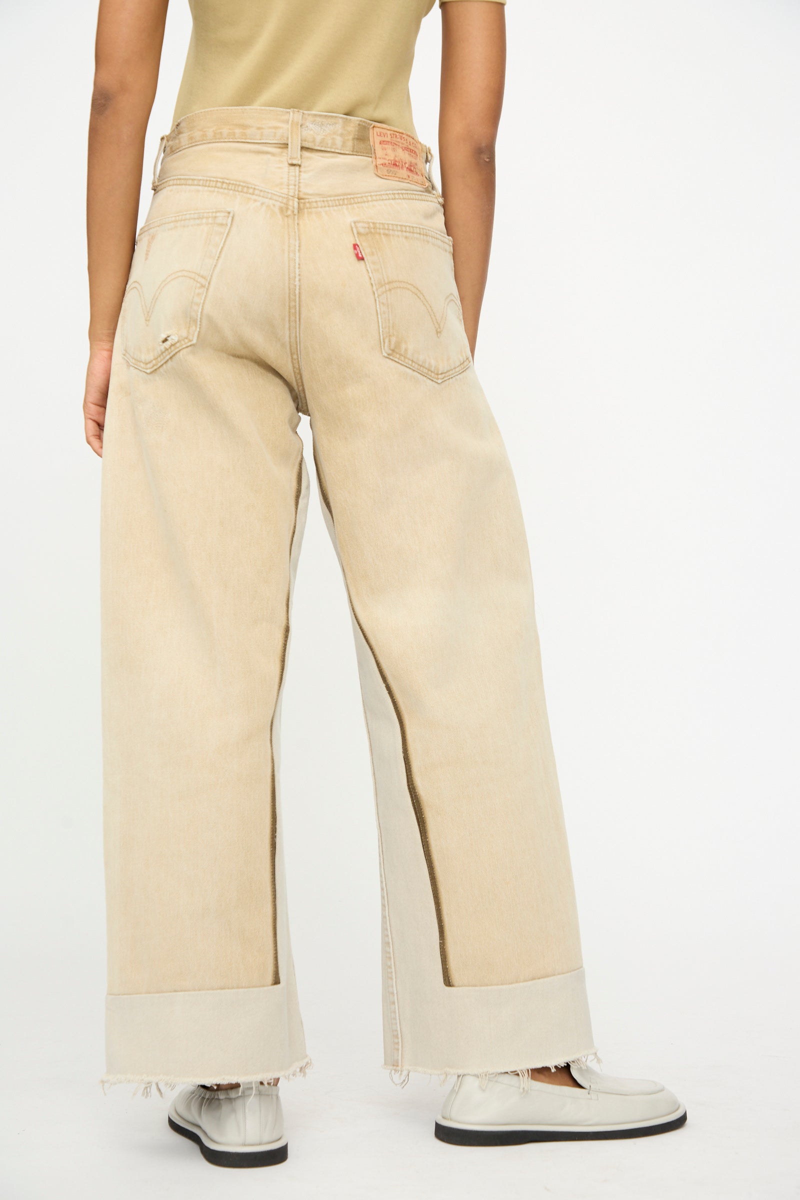 Model wears B Sides Reworked Vintage Culotte in Khaki, a relaxed fit, wide-leg jean with rolled cuffs, paired with white shoes, shown from the back against a plain background.