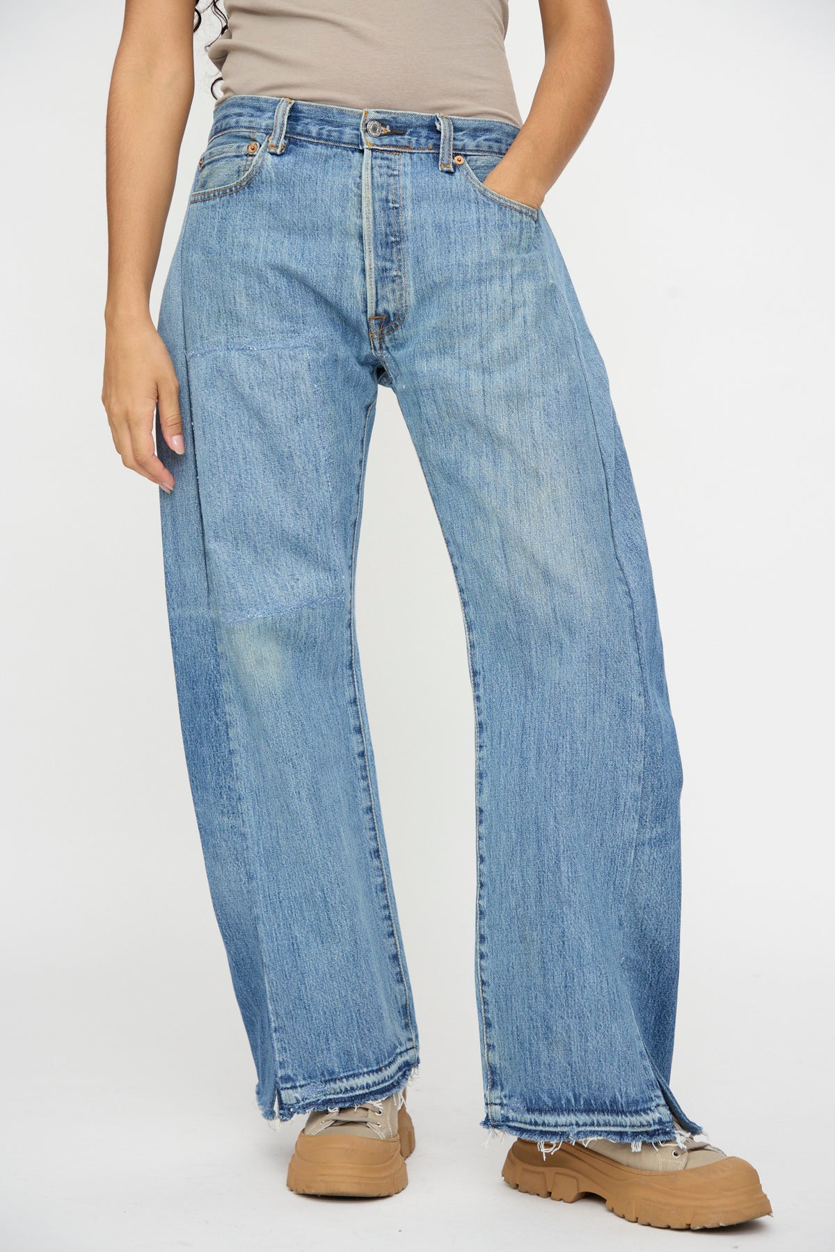 Person wearing B Sides Reworked Vintage Open Hem Slouch in Indigo jeans with a beige top and tan platform shoes, standing against a plain white background.