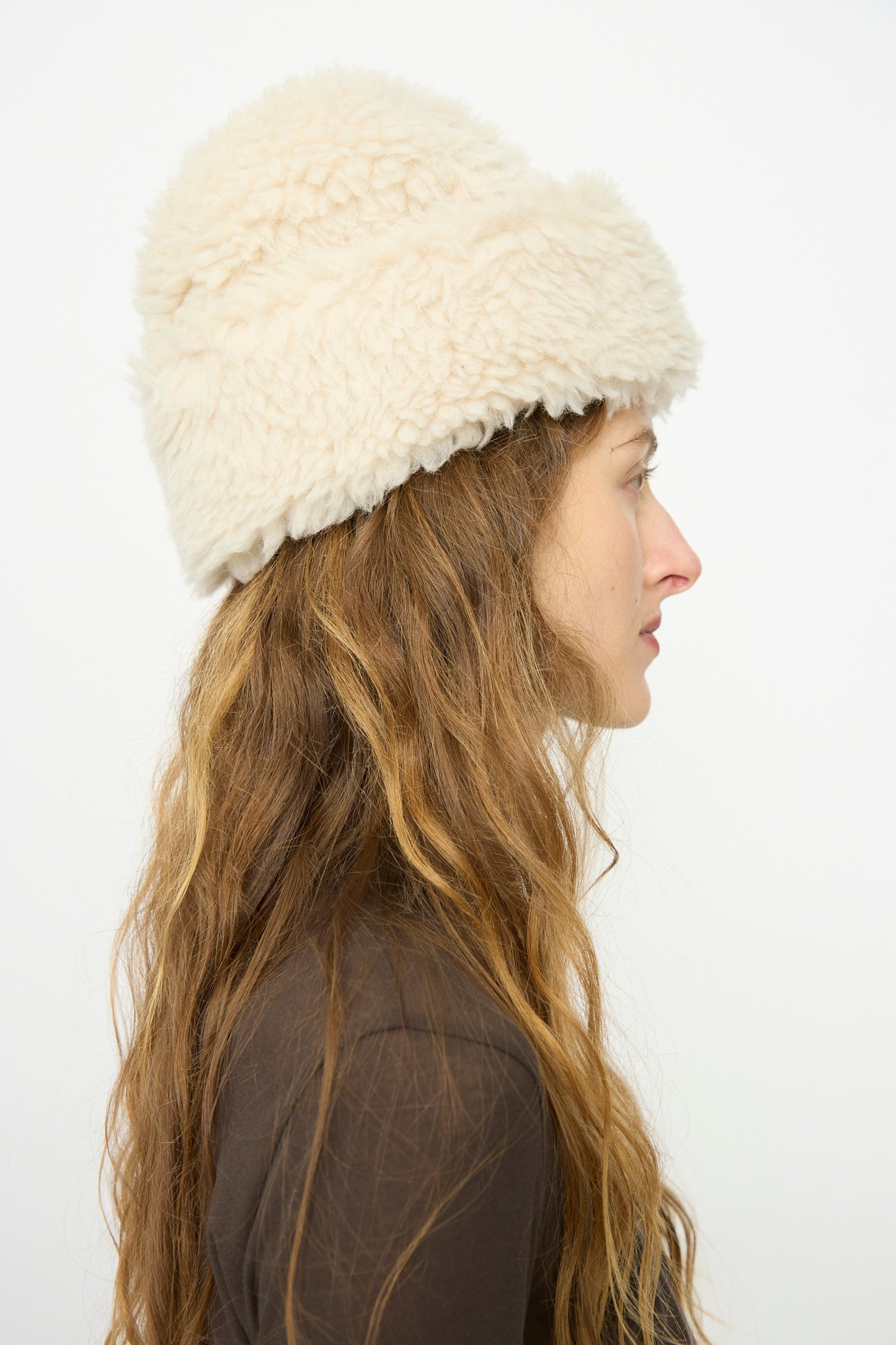 A woman with long wavy hair wears a B Sides Sherpa Hat in Ivory and a brown top, shown in profile against a plain white background.