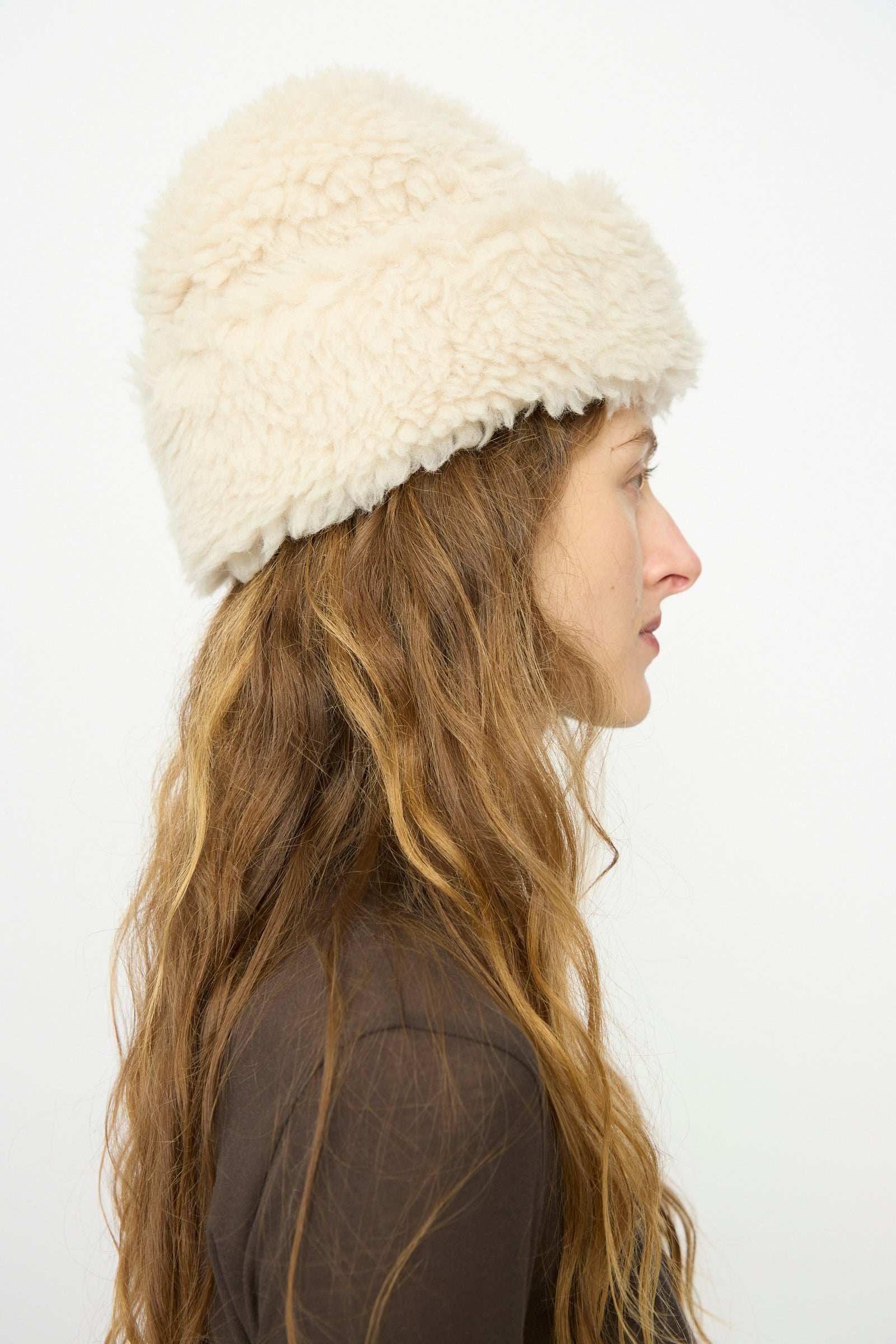 A woman with long wavy hair wears a B Sides Sherpa Hat in Ivory and a brown top, shown in profile against a plain white background.
