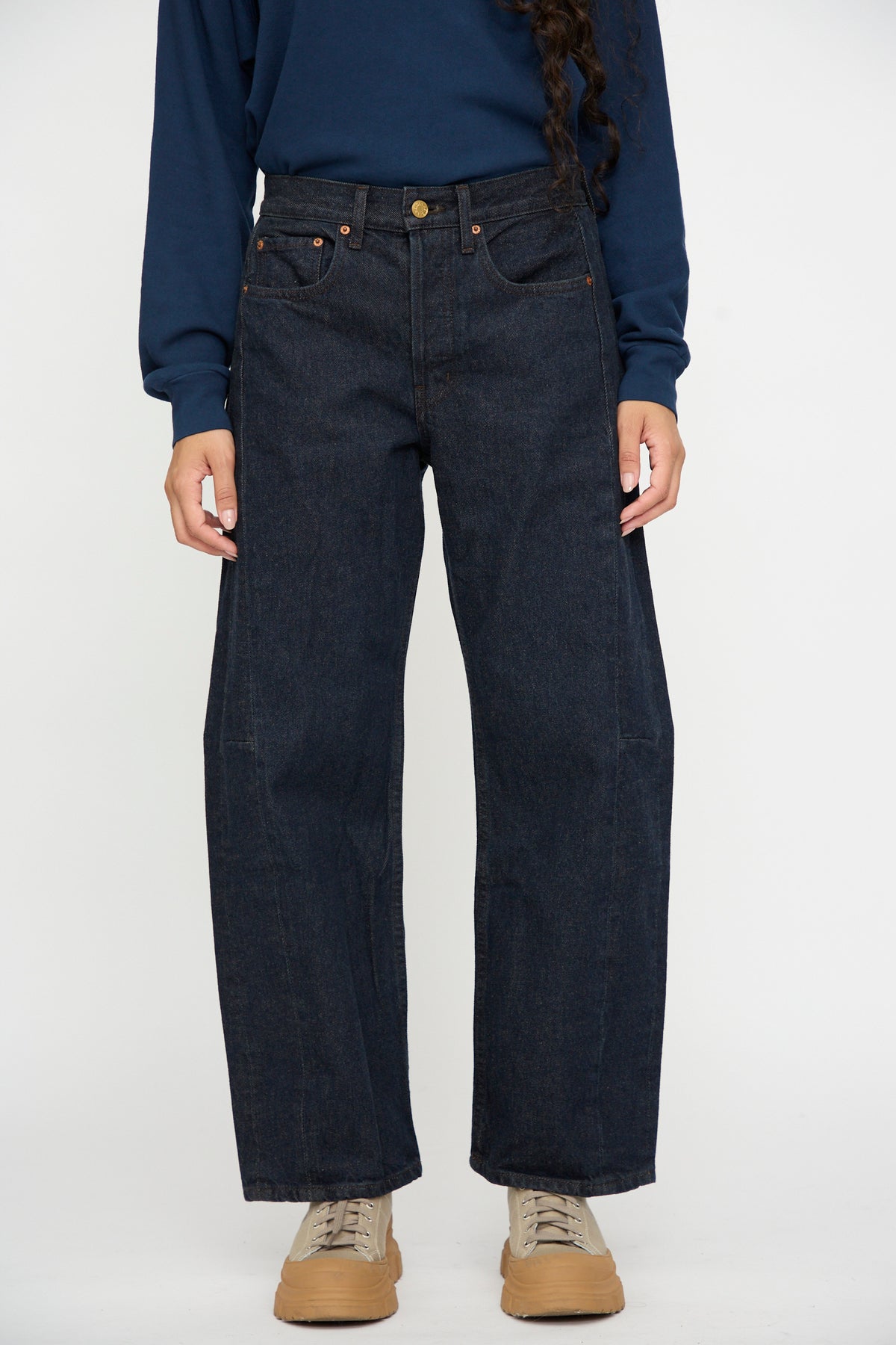 Model wears B Sides Slim Lasso in Indigo Brown Rinse, navy long-sleeve shirt, and tan shoes; only the lower half is shown against a white background.