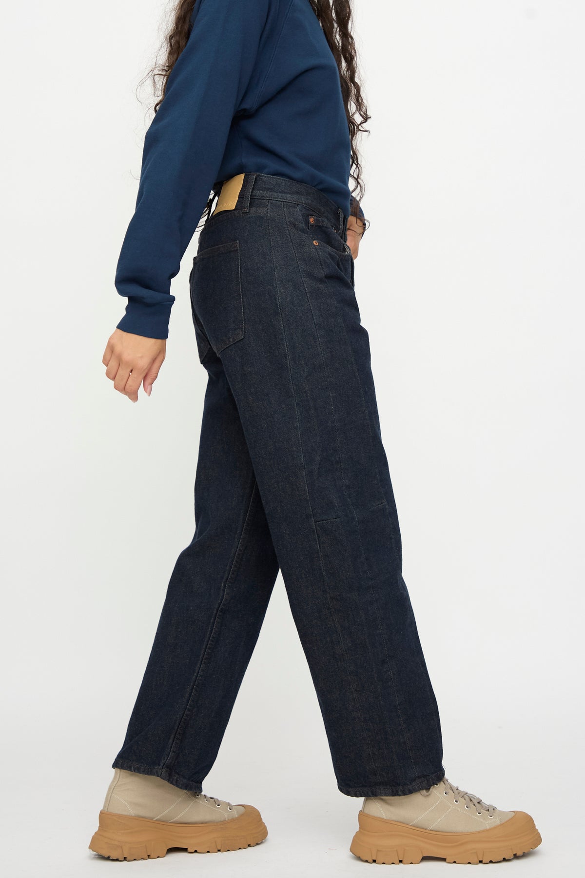 Model wearing Slim Lasso in Indigo Brown Rinse by B Sides, long-sleeve navy shirt, and beige lace-up boots, shown side view against white background.