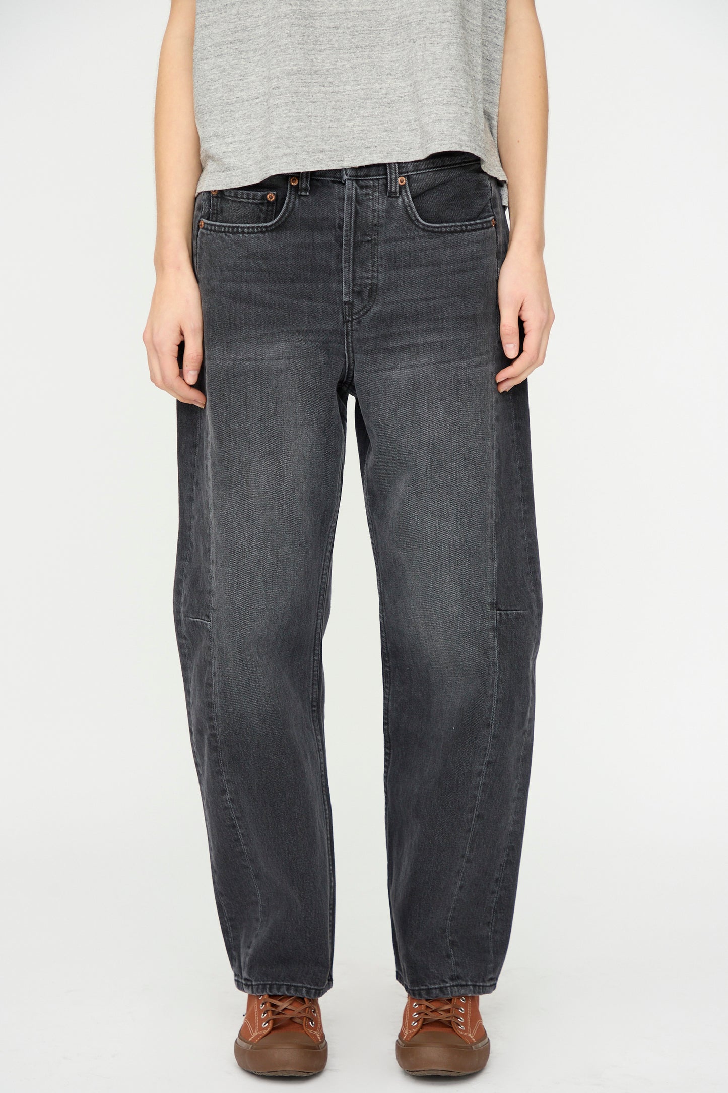 A person stands against a plain white background wearing a gray t-shirt, brown shoes, and B Sides Slim Lasso Jean in Stil Black.