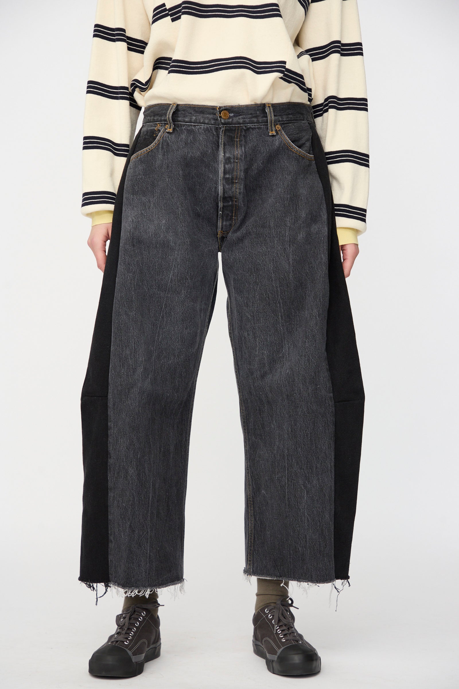 A person wears a striped long-sleeve shirt, B Sides Vintage Lasso Jean in Black with frayed hems, and black shoes, standing against a plain background.