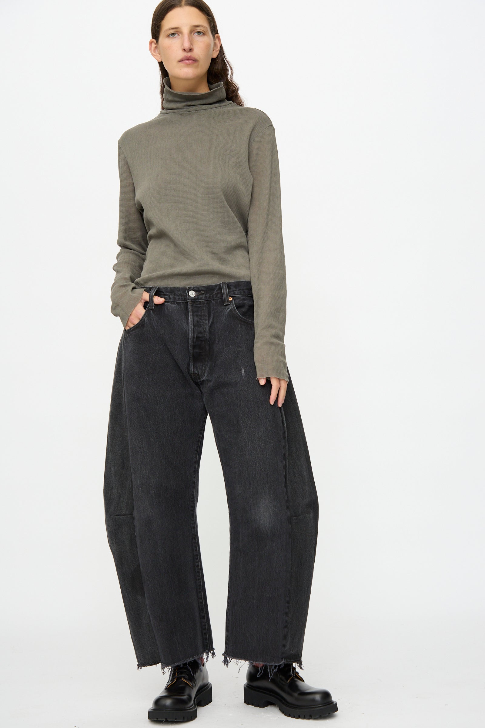 A person stands against a white background wearing a gray turtleneck, black shoes, and B Sides Vintage Lasso Jean in Black with a relaxed fit and frayed hems.