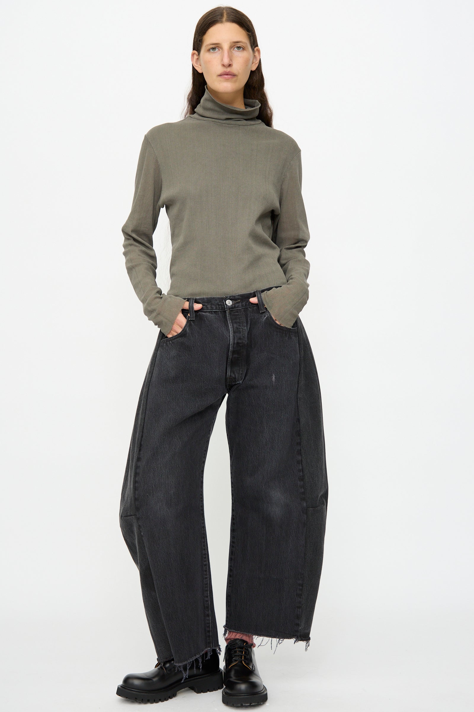 A person stands against a white background, wearing a gray turtleneck and B Sides’ Vintage Lasso Jean in Black—wide-leg, vintage-style denim with raw hems and relaxed fit—paired with black shoes and hands in their pockets.