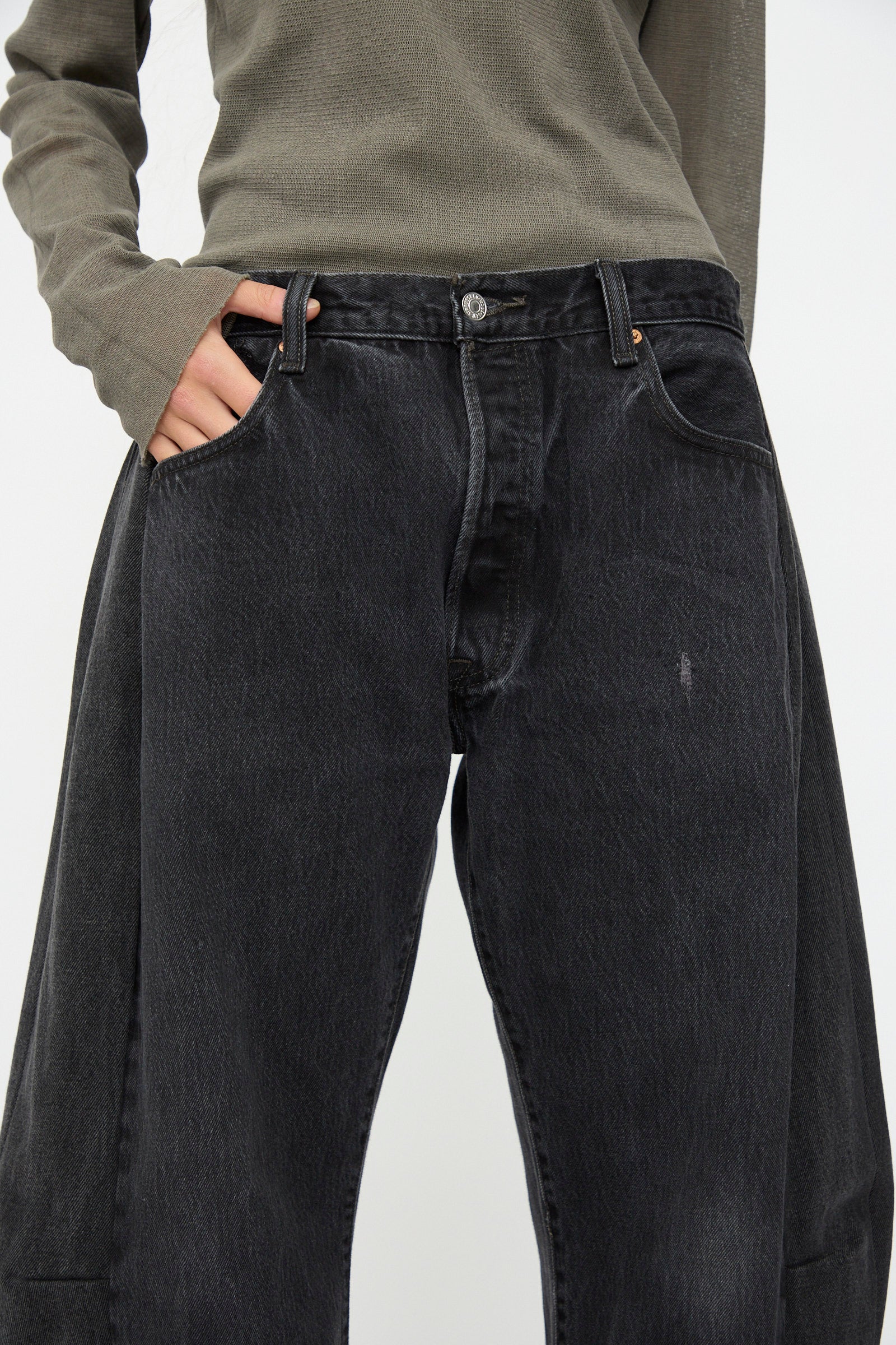 Person wearing a long-sleeved, olive-green top and B Sides Vintage Lasso Jean in Black with one hand in a pocket.