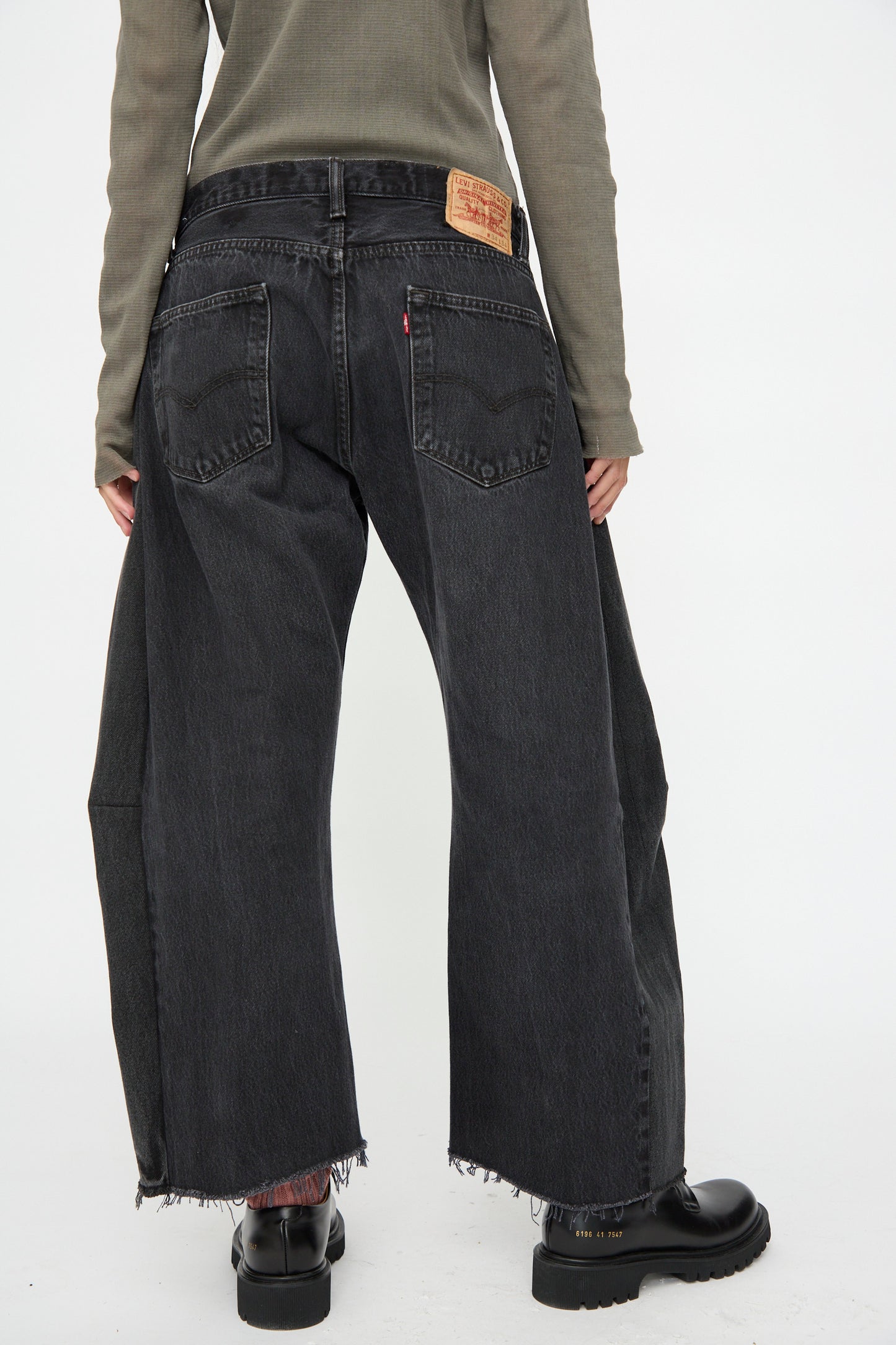 Person wearing B Sides Vintage Lasso Jean in Black, relaxed fit with frayed hems, paired with a green long-sleeve top and black shoes; photographed from the back against a plain white background.
