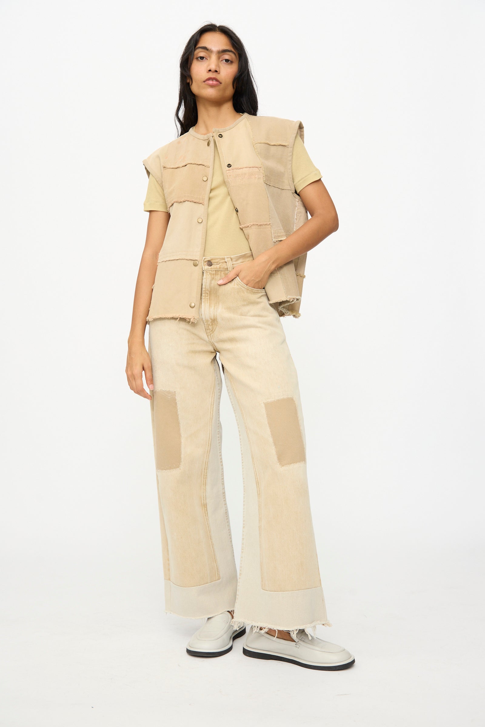 A person stands against a plain background wearing the B Sides Vintage Madras Vest in Khaki, a yellow T-shirt, wide-leg jeans with repurposed denim patches, and white platform shoes.