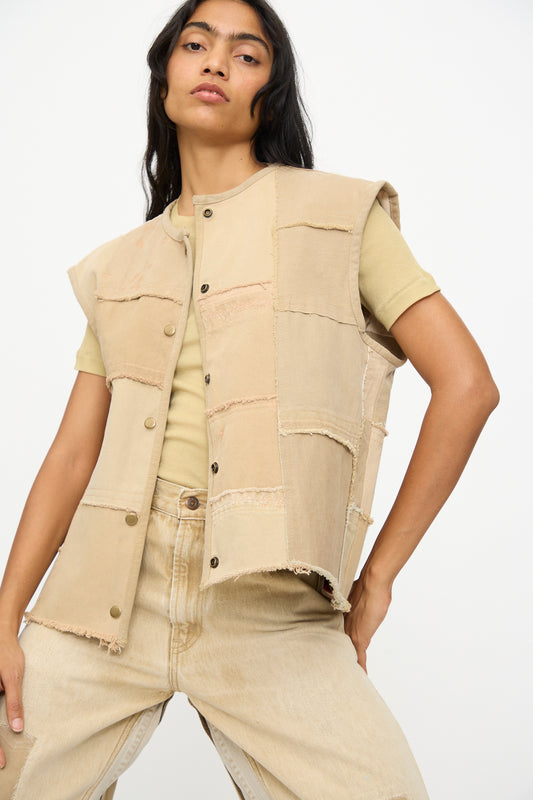 Model wears the B Sides Vintage Madras Vest in Khaki over a light yellow t-shirt and beige jeans, posing with hand on hip against a plain background.