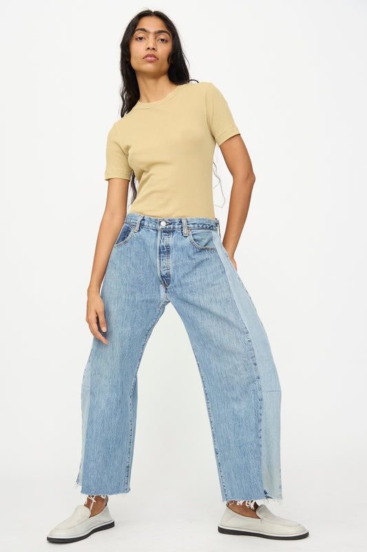 A person wears a beige short-sleeve top, B Sides Vintage Reworked Lasso Jean in Indigo, and white slip-on shoes while standing against a plain white background.