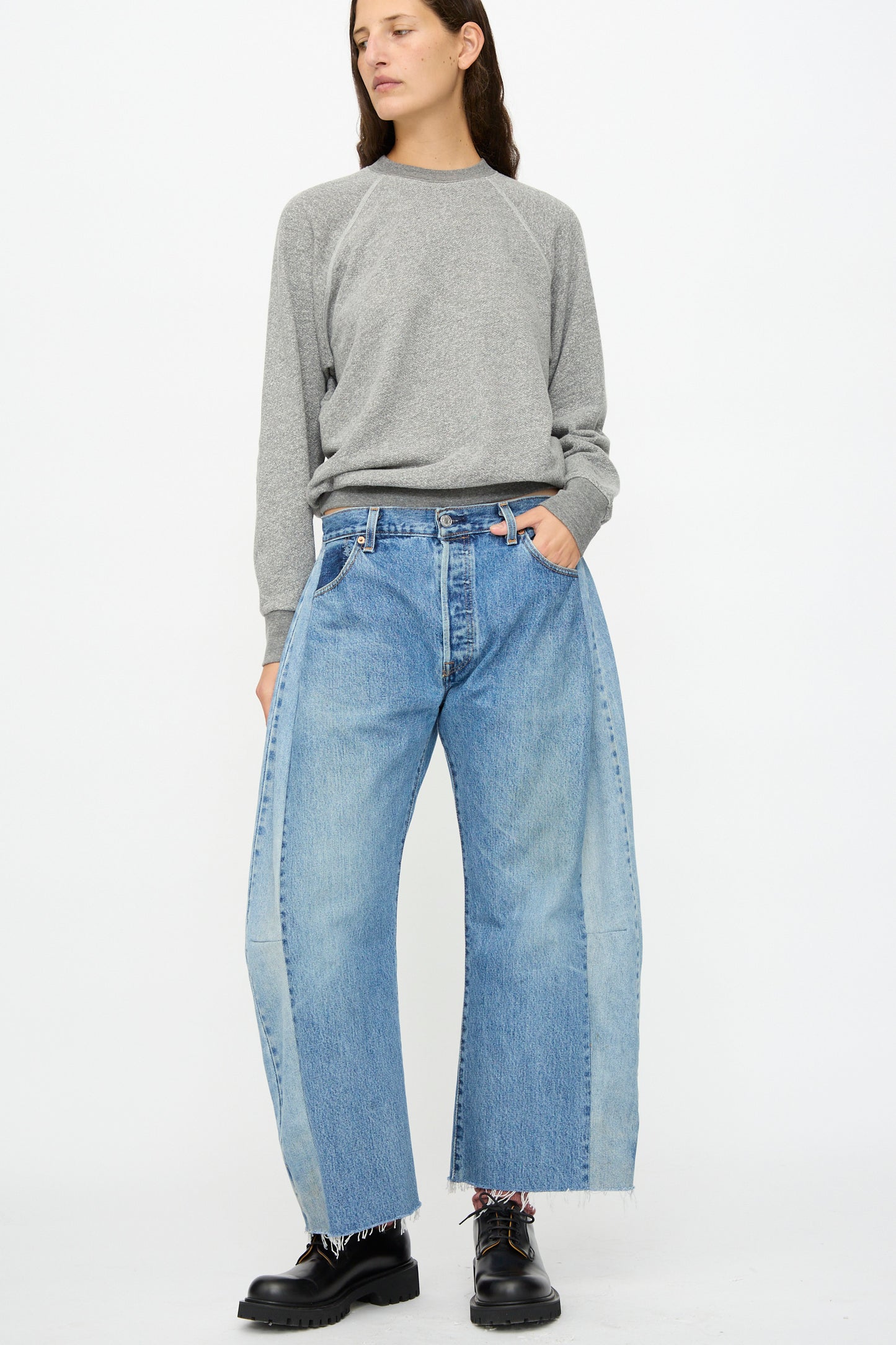 Person wearing a grey long-sleeve shirt, B Sides Vintage Lasso Jean in Indigo, and black platform shoes stands against a plain white background.