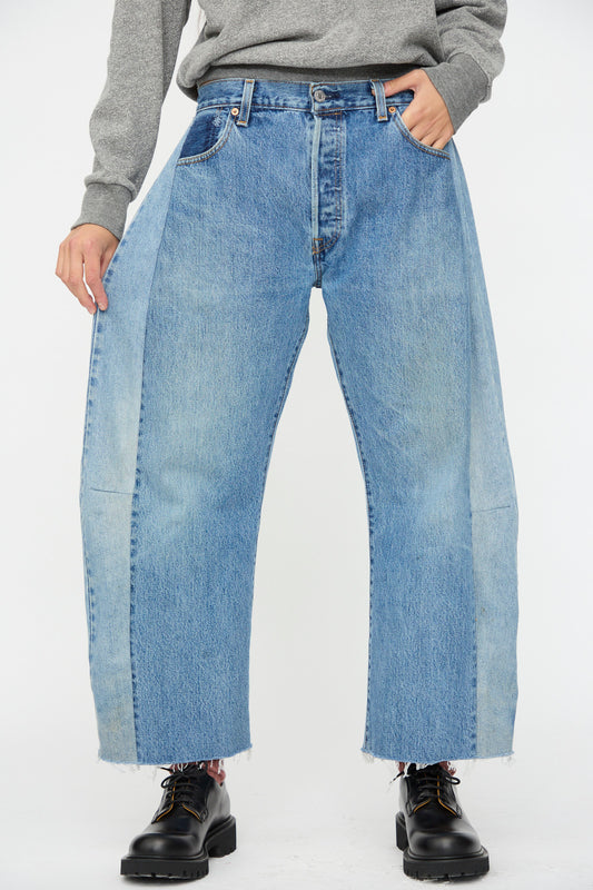 Person wears B Sides Vintage Lasso Jean in Indigo with raw hems, styled with a grey sweater and black lace-up shoes, set against a plain background.