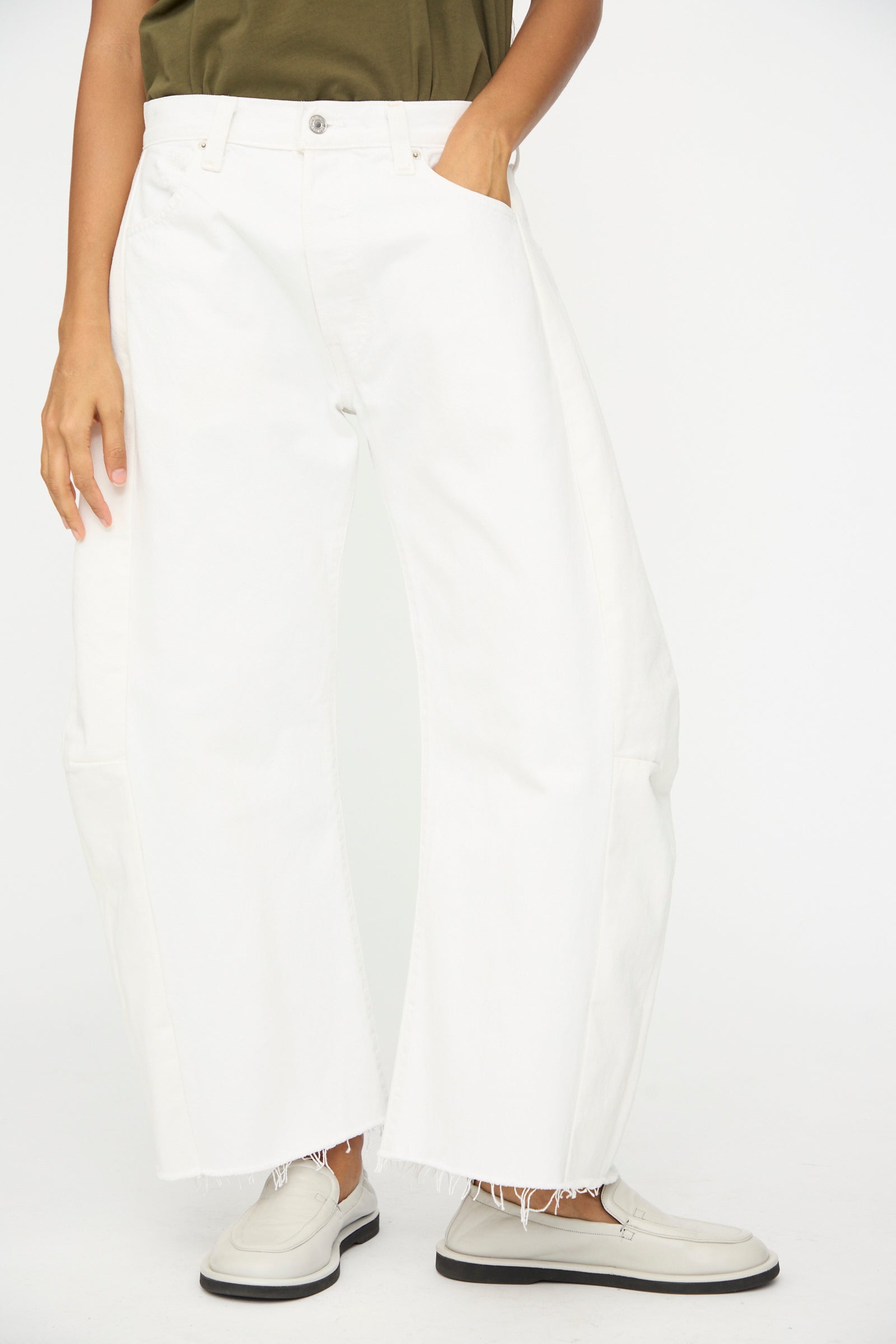 Model wears B Sides Vintage Reworked Lasso Jean in White with off-white loafers, one hand in pocket, standing against a plain white background.