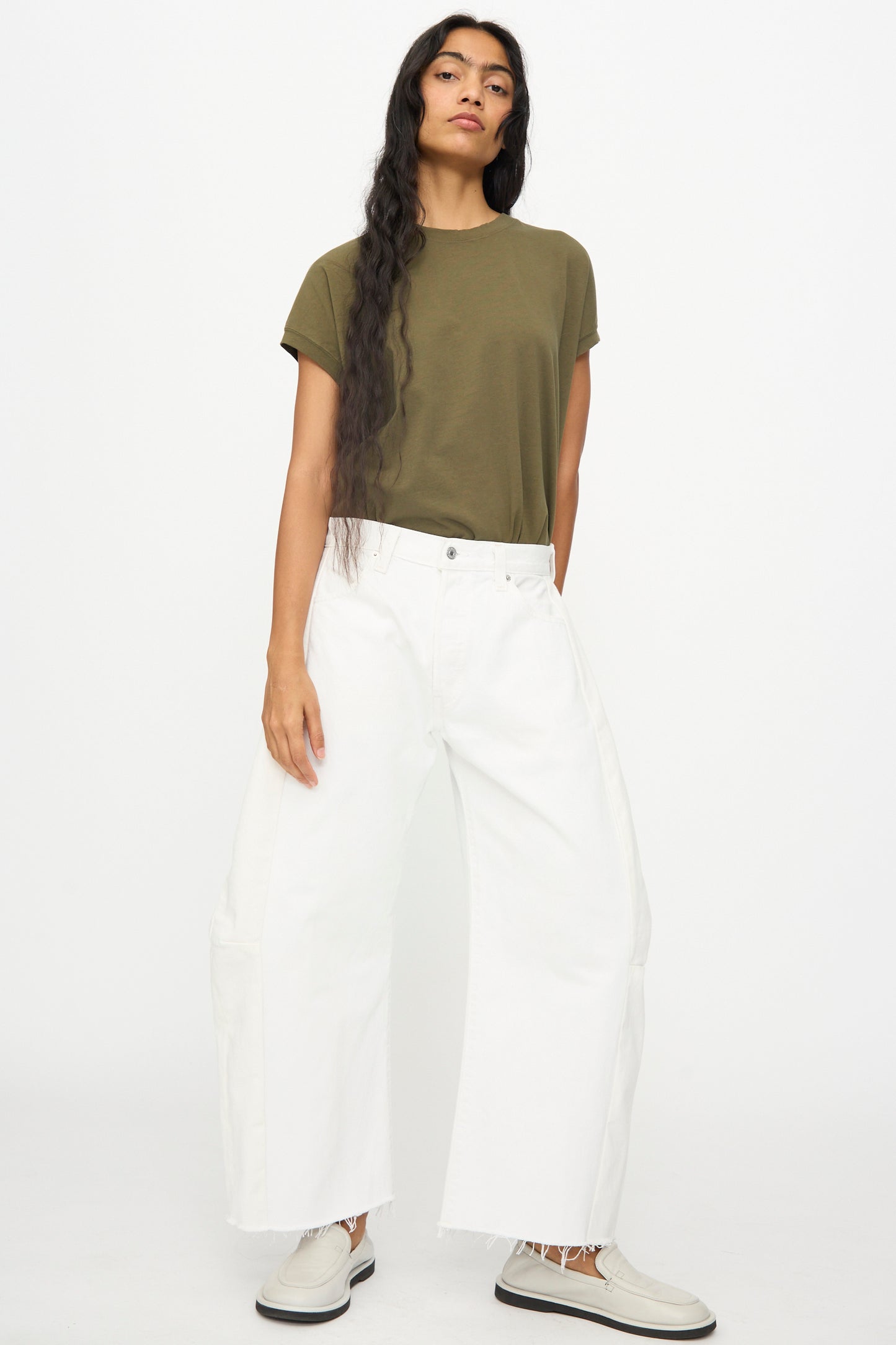 A person stands against a plain background wearing a green short-sleeve t-shirt, light-colored shoes, and B Sides' Vintage Reworked Lasso Jean in White.