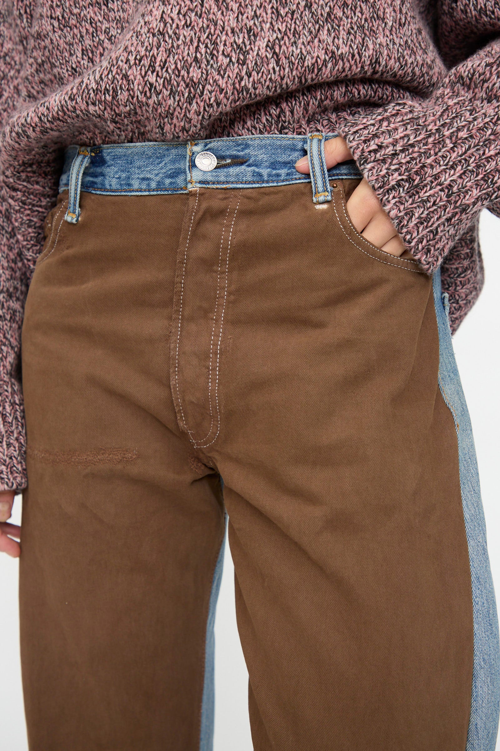 Person wears B Sides Vintage Straight Rework Halfsie jeans in brown and indigo with a pink and gray textured sweater, hand in pocket.