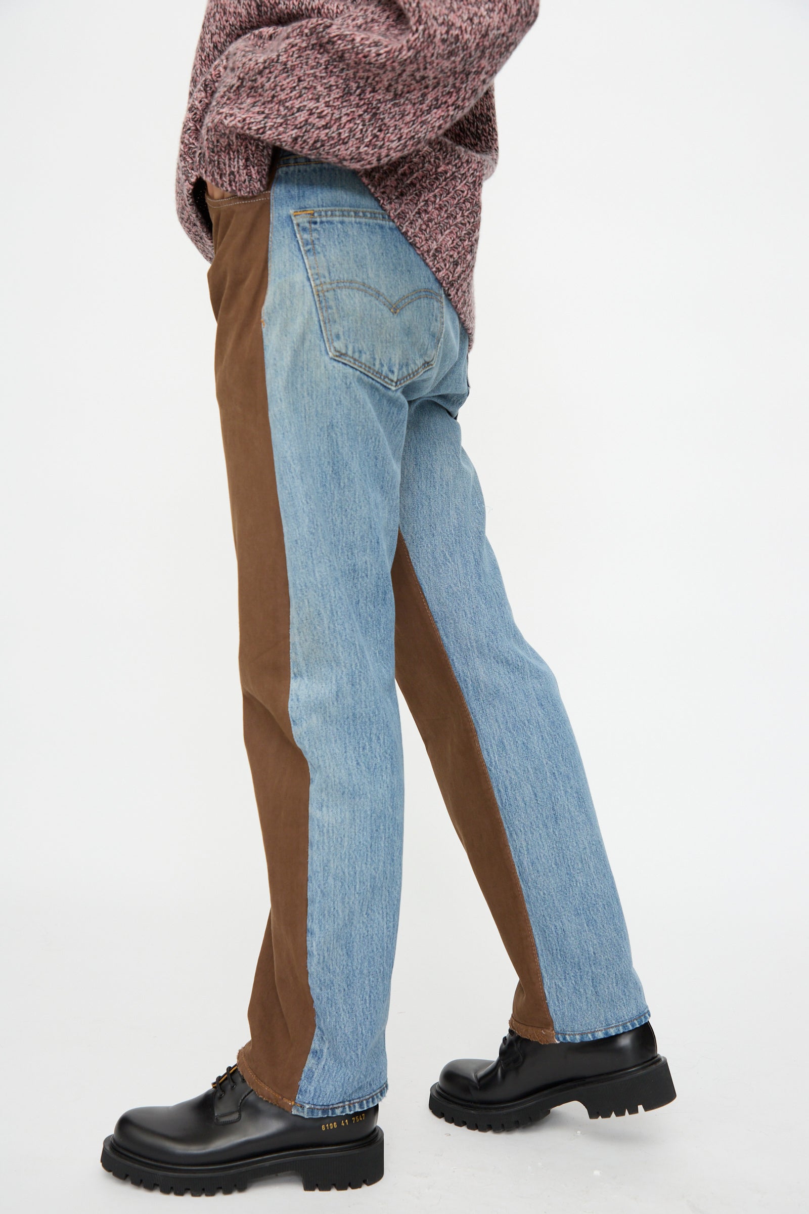 Model wears the B Sides Vintage Straight Rework Halfsie in Brown and Indigo—mid-rise, 100% cotton denim—with a textured maroon sweater and black lace-up shoes, shown from the side against a plain background.