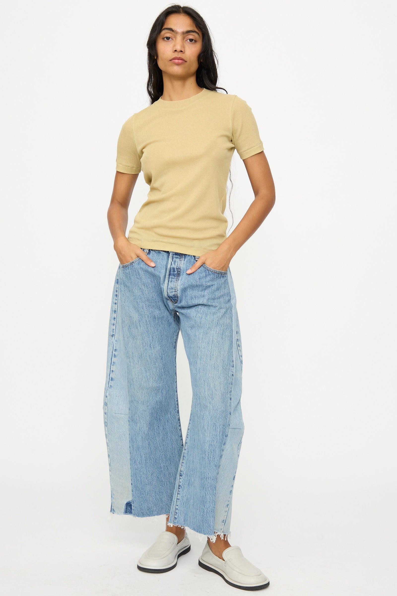 A woman stands against a white background wearing the B Sides Vivien Rib Tee in Honey, light blue wide-leg jeans, and white slip-on shoes, with her hands in her pockets.