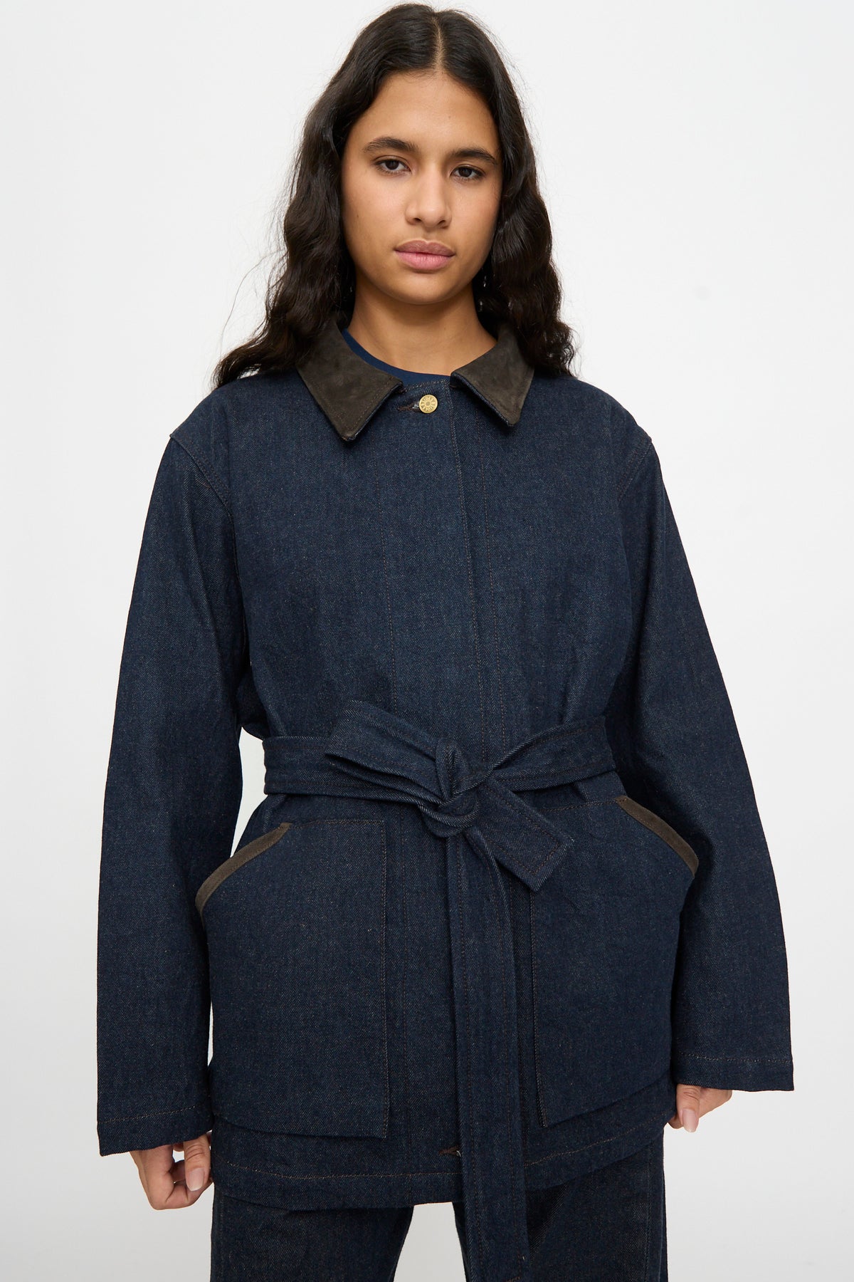 A person wears the B Sides Workwear Jacket in Indigo Rinse and Espresso Suede, standing against a plain light background.