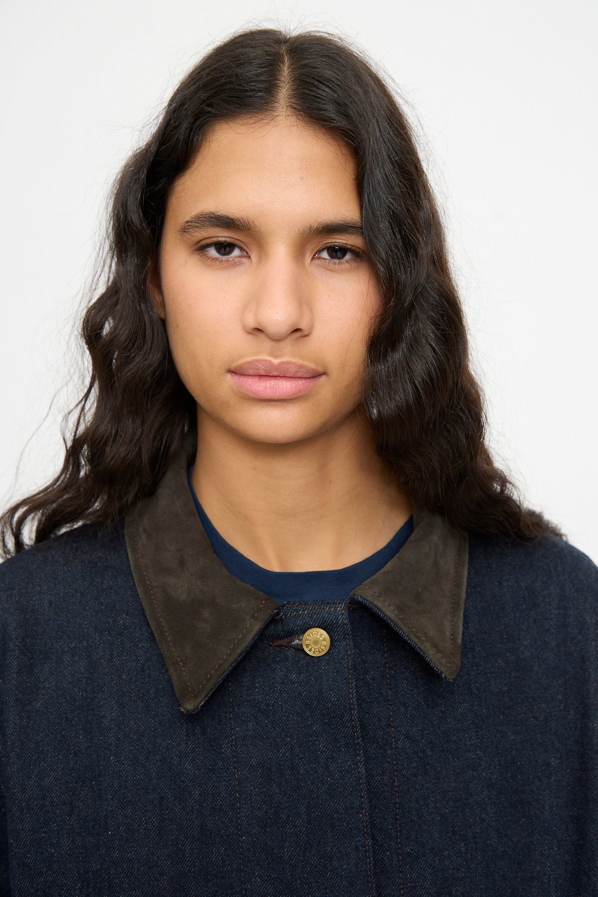 A person with long dark wavy hair wears the B Sides Workwear Jacket in Indigo Rinse and Espresso Suede, standing against a plain white background.