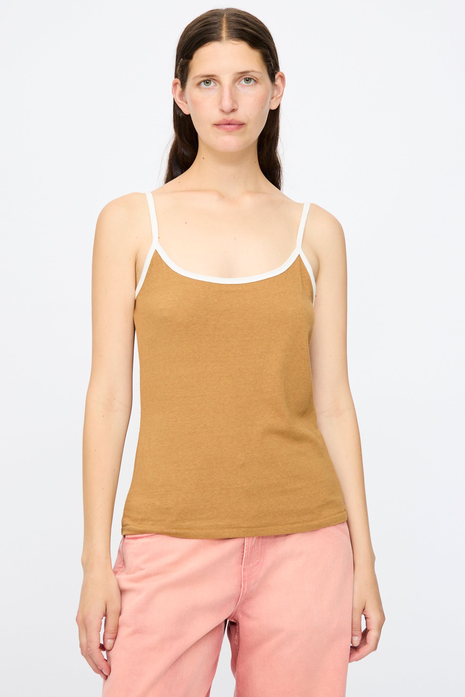 A woman stands facing forward in the B Sides Zora Ringer Tank in Camel and White, a lightweight cotton silk blend top with white straps, paired with pink pants against a plain light background.