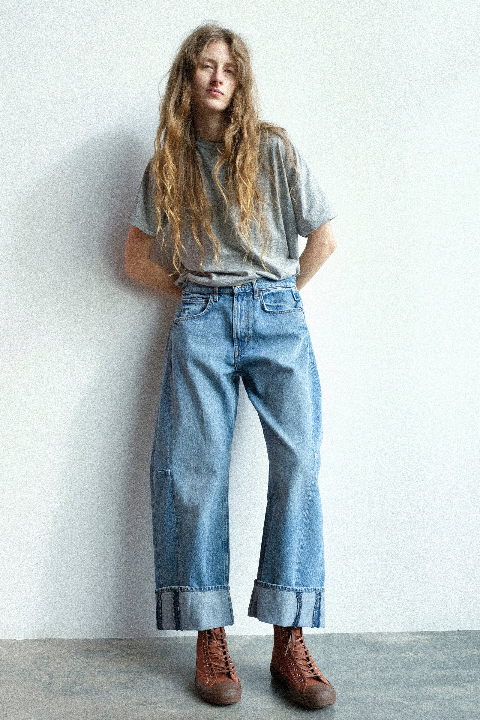 A woman leaning against the a white wall wearing B Sides top and bottom.