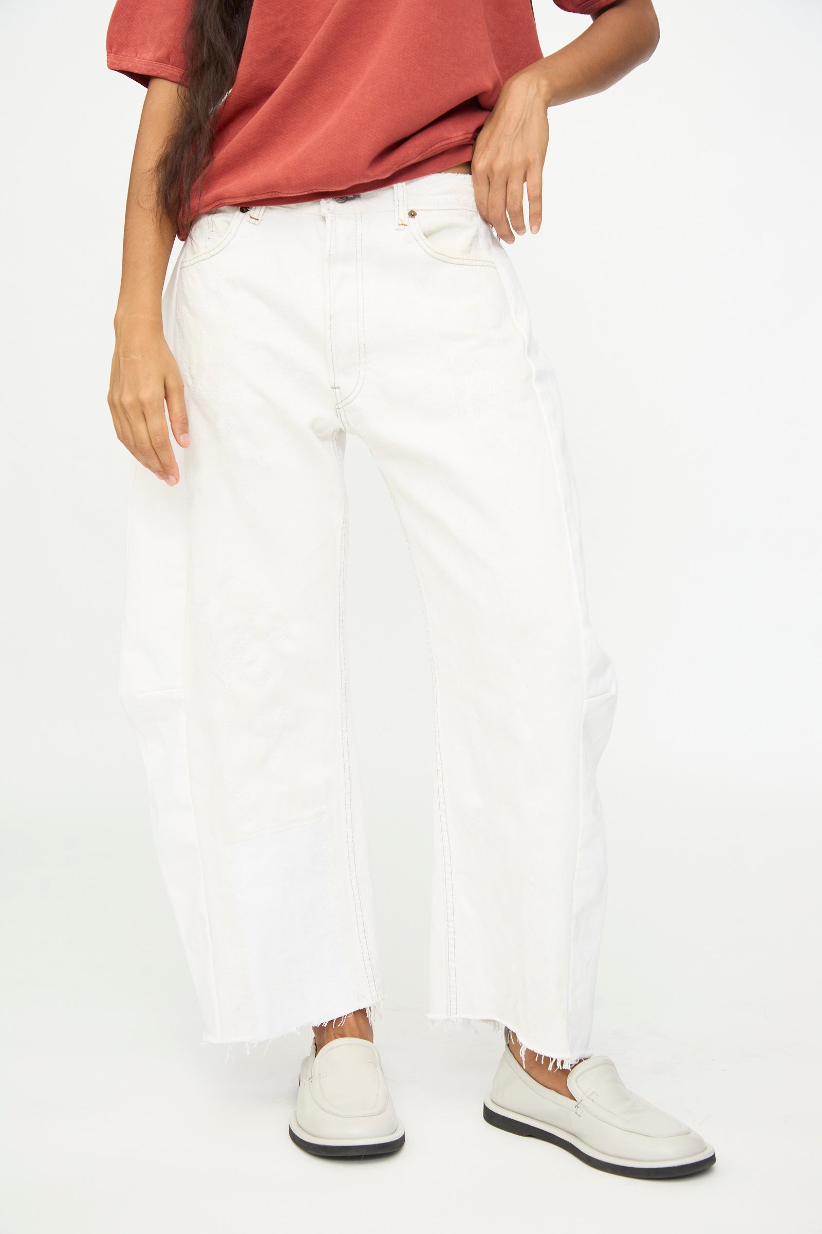 A person wearing a red t-shirt, B Sides Vintage Reworked Lasso Jean in White, and white slip-on shoes, standing against a plain white background.