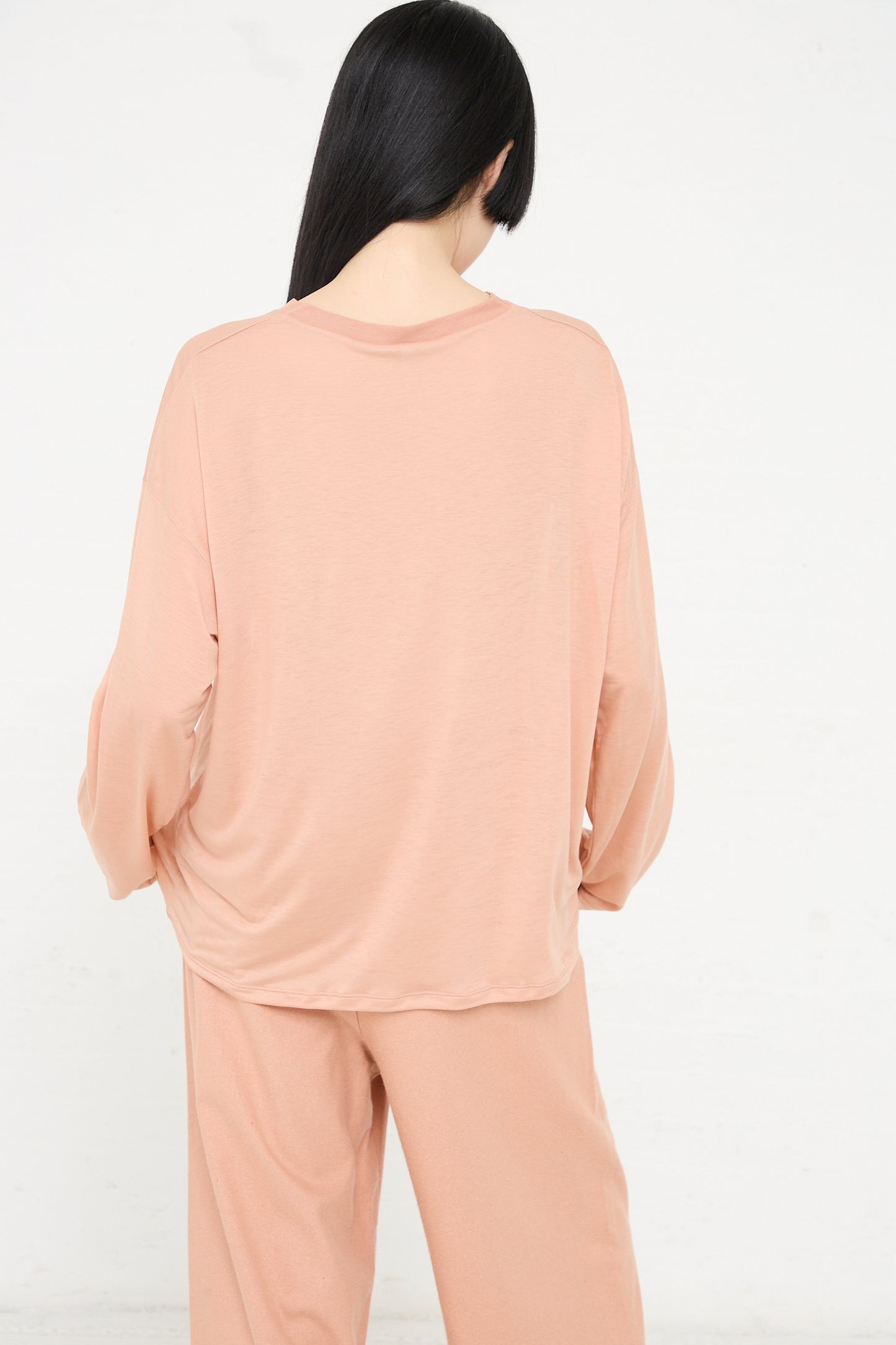 Woman wearing a Baserange Bamboo Loose Long Sleeve Tee in Yu Rose and matching pants, viewed from behind.