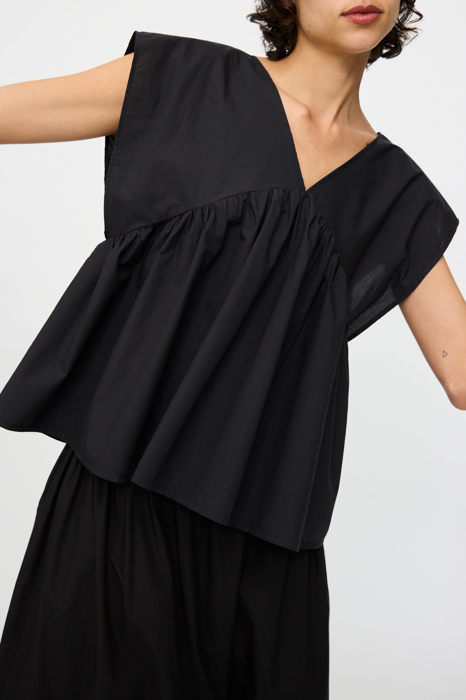 A person wears the Baserange Cable Top in Black—an oversized, sleeveless organic cotton top with gathered chest and wide shoulders—paired with a black skirt against a plain, light background.