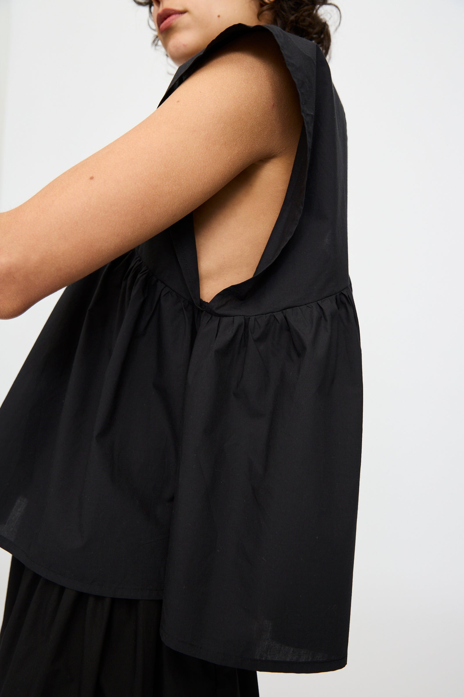 A model wears the Baserange Cable Top in Black—an oversized, sleeveless style with wide armholes and a gathered back—shown from the side against a plain backdrop.