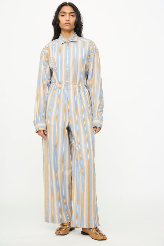 A person stands against a plain background, wearing Baserange's Claude Pants in Grid Stripe—loose-fitting, organic cotton pull-on wide leg pants—paired with a matching striped long-sleeved shirt and brown shoes.