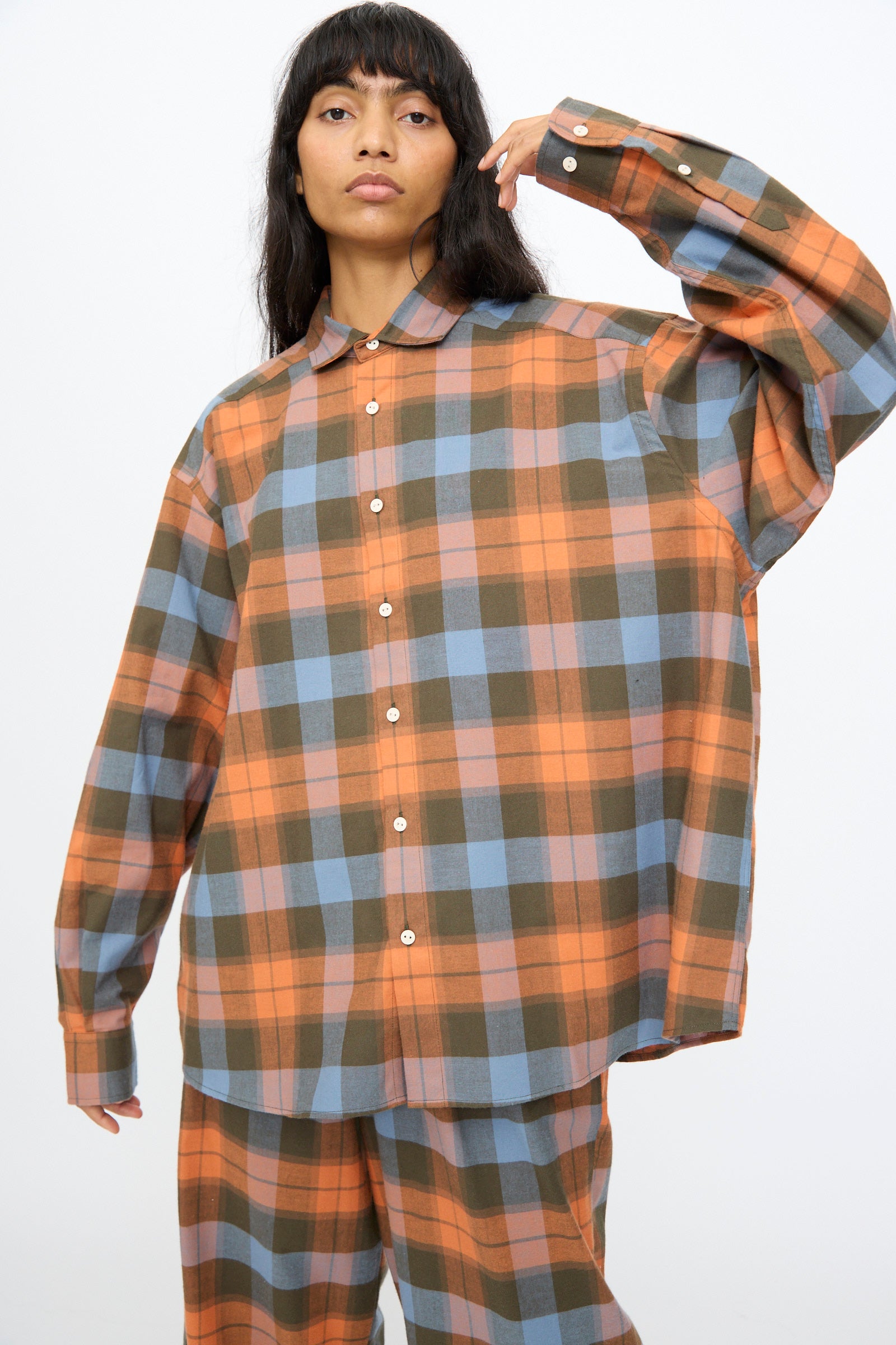 A person wearing the Baserange Claude Shirt in Frame Plaid, featuring oversized orange, blue, and olive green checks, stands against a plain background.