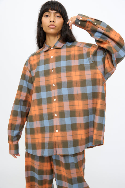 A person wearing the Baserange Claude Shirt in Frame Plaid, featuring oversized orange, blue, and olive green checks, stands against a plain background.