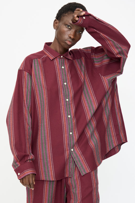 Model wears the Baserange Claude Shirt in Maroon Stripe, a loose-fitting, long-sleeve button-up with multicolored vertical accents, paired with matching pants, standing against a plain white background.