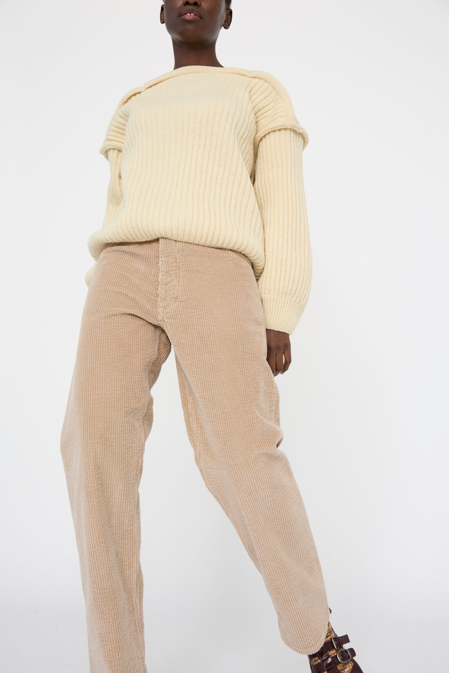 A person in a cream sweater and Baserange's Corduroy Indre Pant in Sand stands against a white background.