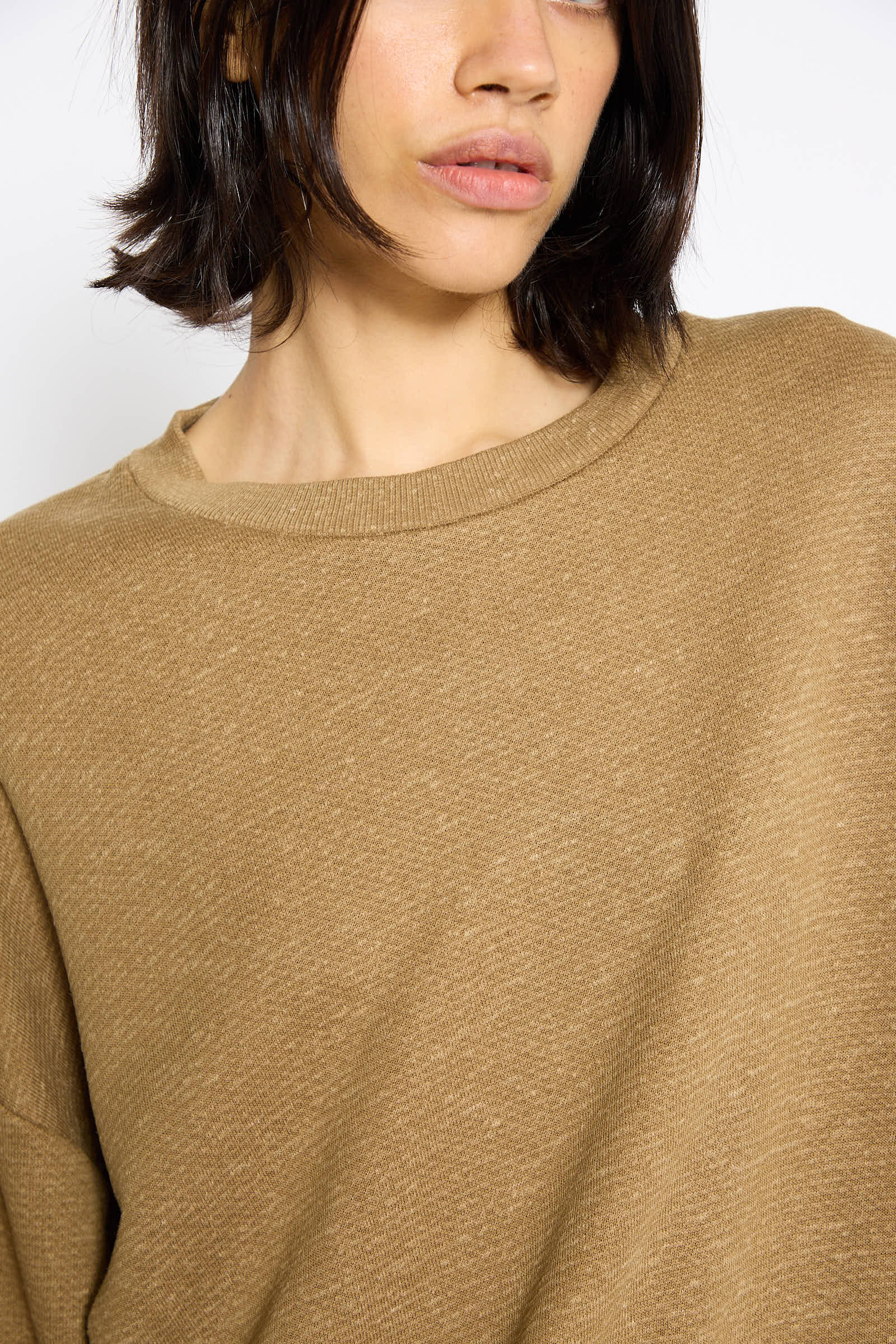 A person with shoulder-length dark hair, wearing a Baserange Cotton Fleece Rim Sweatshirt in Stone Green made from regenerative cotton, is partially visible against a white background.