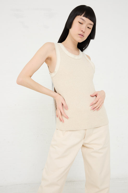 A woman with black hair in a Baserange Organic Cotton Hemp Rib Supple Tank in Undyed and trousers poses with her hands on her hips against a white background.