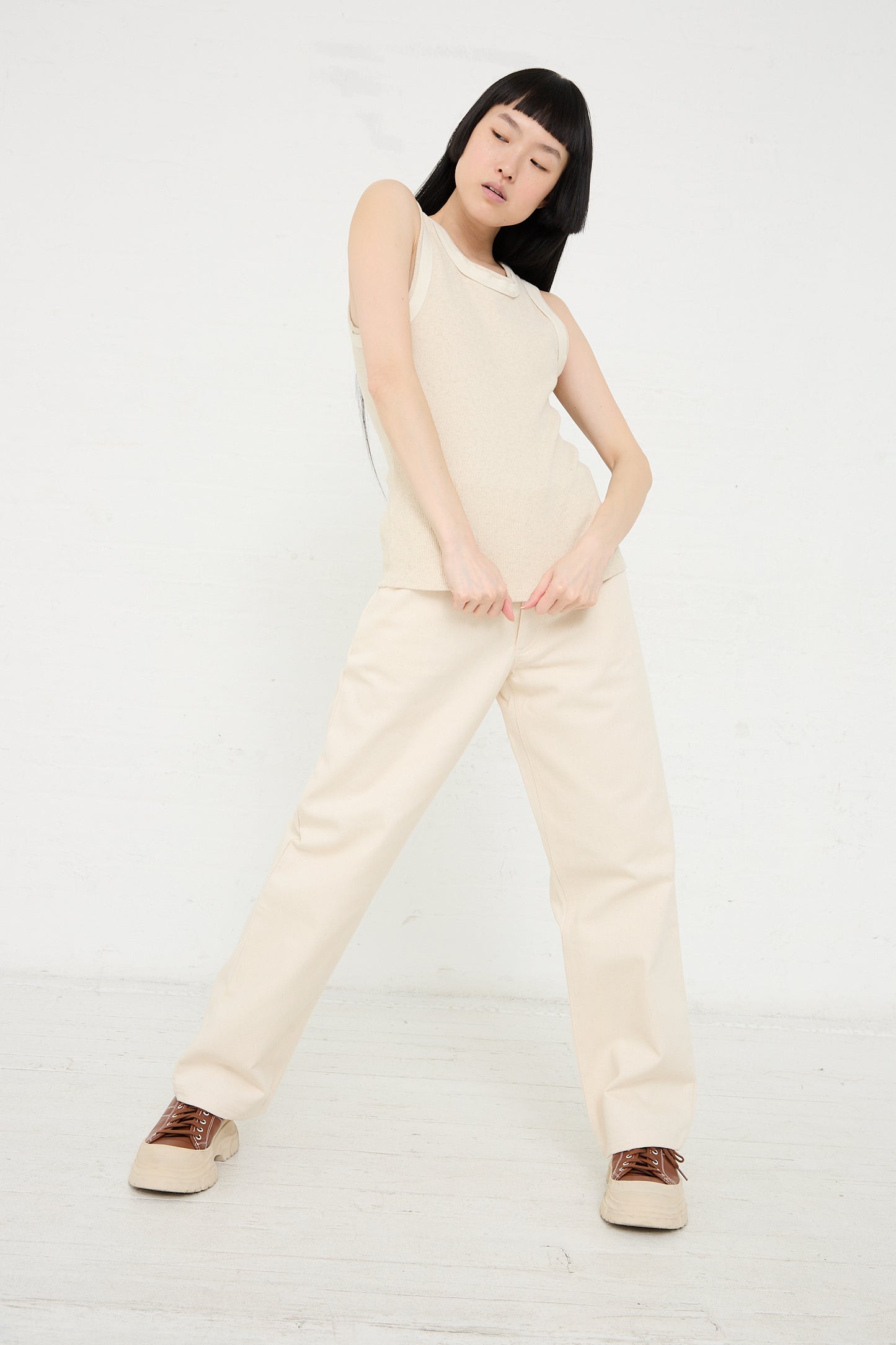 A woman in a Beige Baserange Organic Cotton Hemp Rib Supple Tank in Undyed and trousers poses with her hands on her hips against a white background.