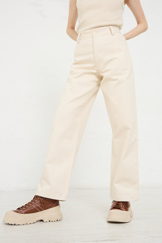 A person standing in a room wearing Baserange's Organic Cotton Indre Pant in Undyed and brown chunky lace-up shoes, viewed from behind.