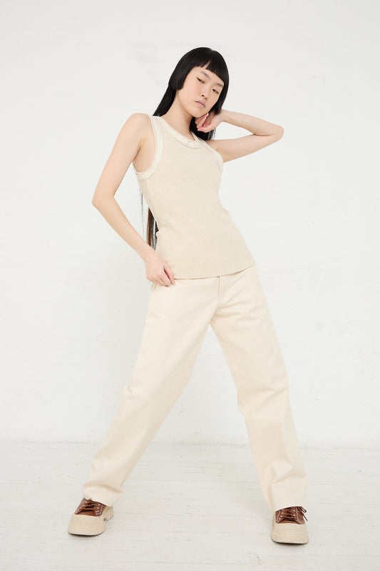 A woman in a sleeveless top and Baserange's Organic Cotton Indre Pant in Undyed posing with one hand on her hip against a white background.