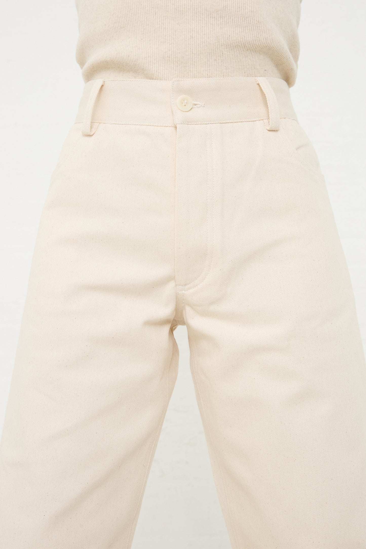 Close-up of a person wearing Baserange's Organic Cotton Indre Pant in Undyed with a button closure and tucked-in sweater, viewed from the front waist down.