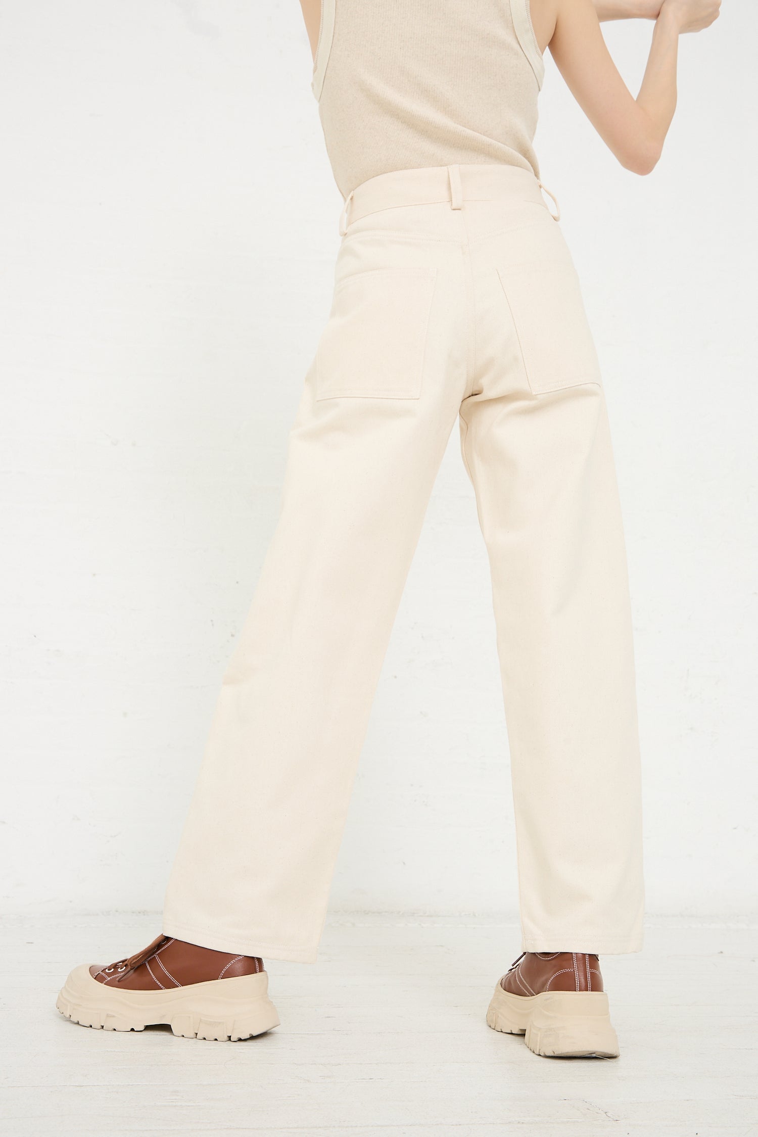 Woman standing in Baserange's Organic Cotton Indre Pant in Undyed and two-tone brown platform shoes, with a partial view of a beige top.